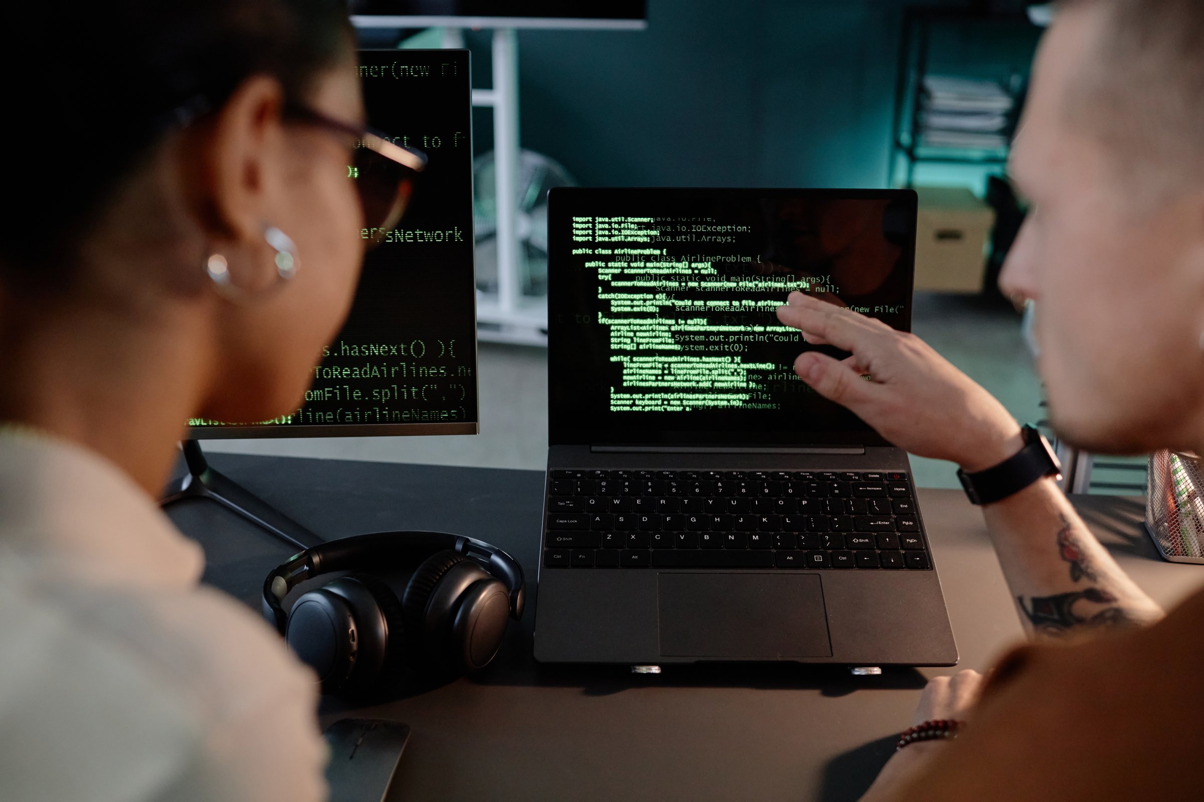Cropped shot of unrecognizable male IT programmer pointing at laptop screen with lines of code running collaborating with female colleague both working late in office