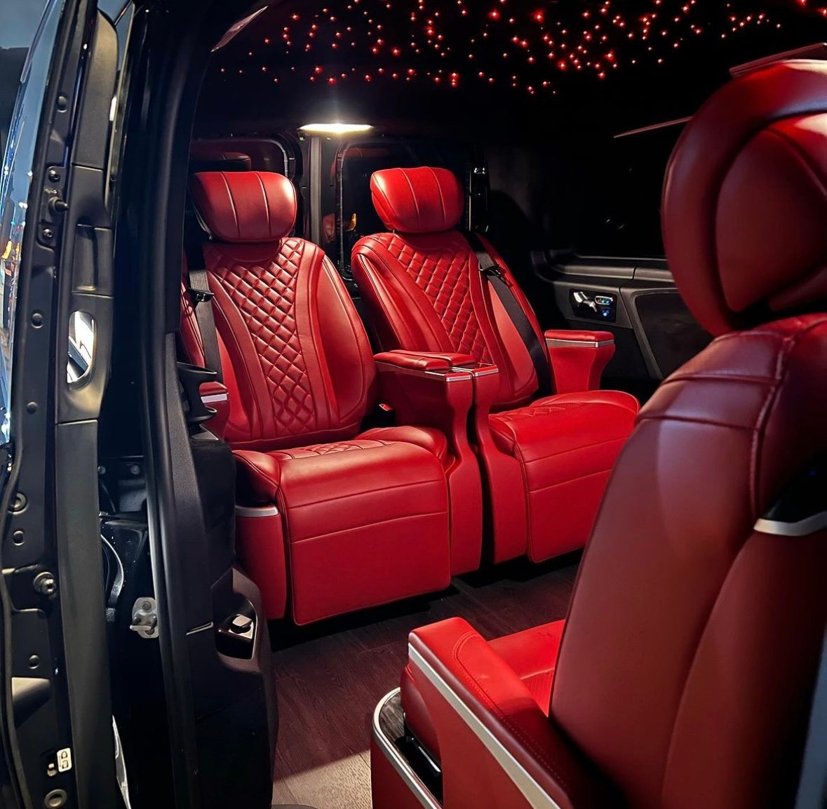 Luxurious vehicle interior with red leather seats and ceiling lights, resembling a starry sky.