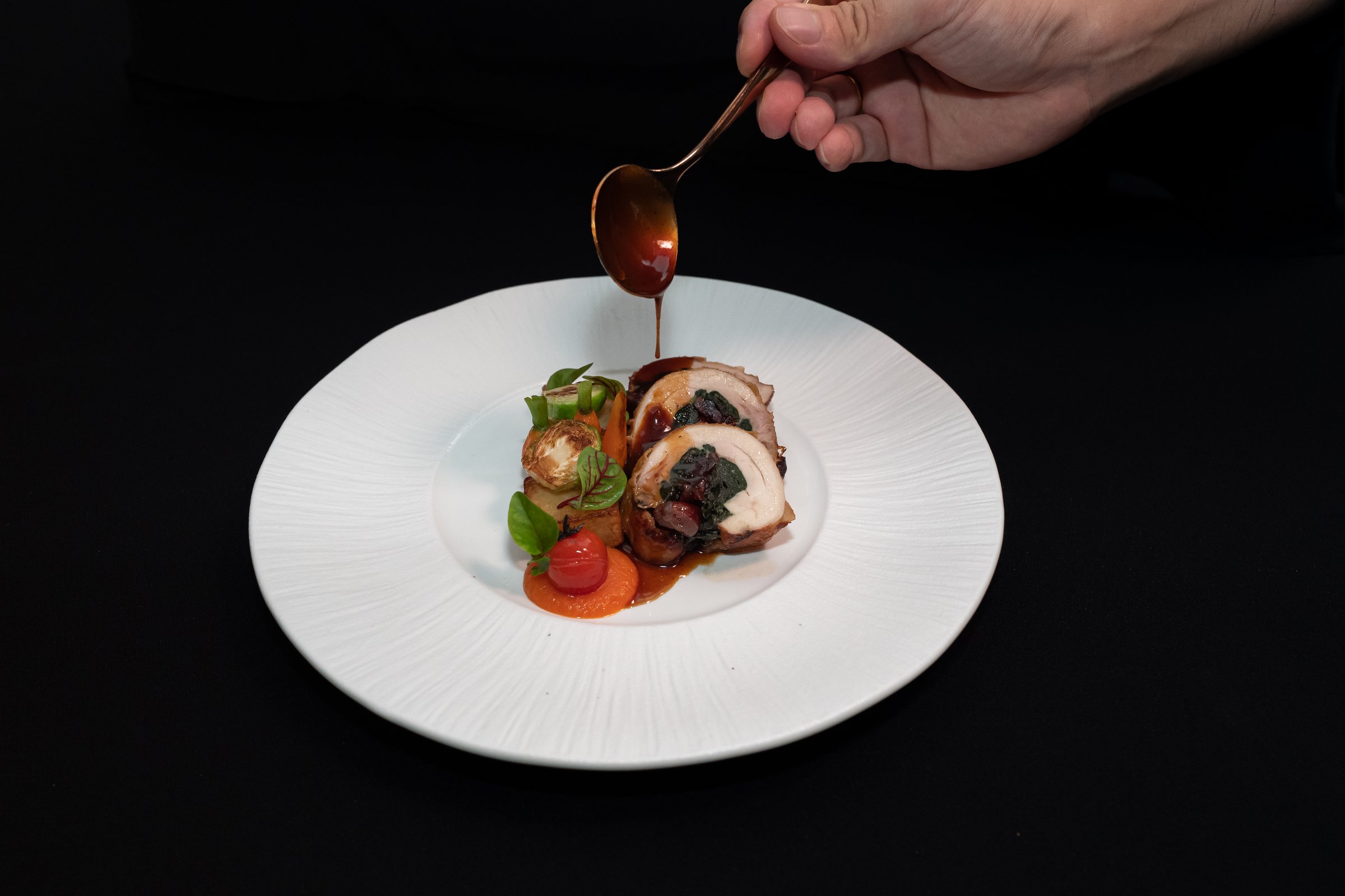 A chef delicately garnishing a beautifully plated gourmet meal, ready to be served. The dish features a medley of colorful ingredients on a textured plate