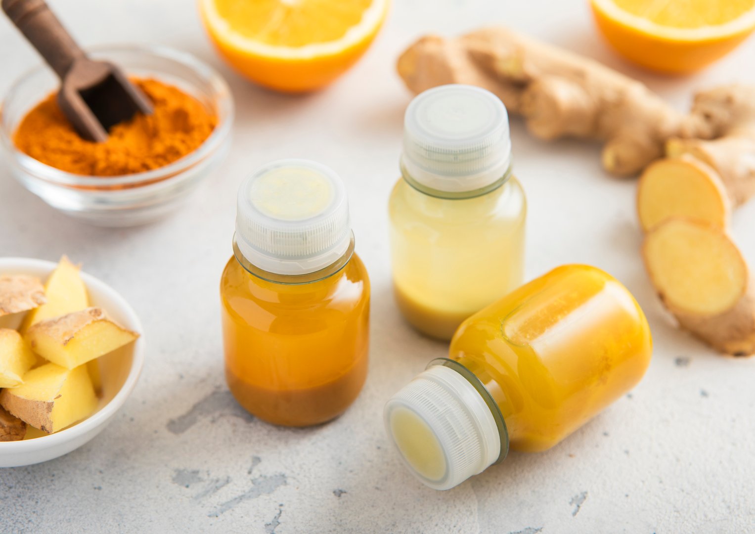 Immune ginger and turmeric energy shot drink with ginger root and turmeric powder on light background.