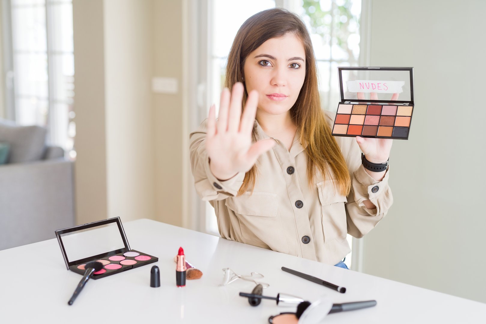 Beautiful young woman using make up cosmetics applying color from palete with open hand doing stop sign with serious and confident expression, defense gesture