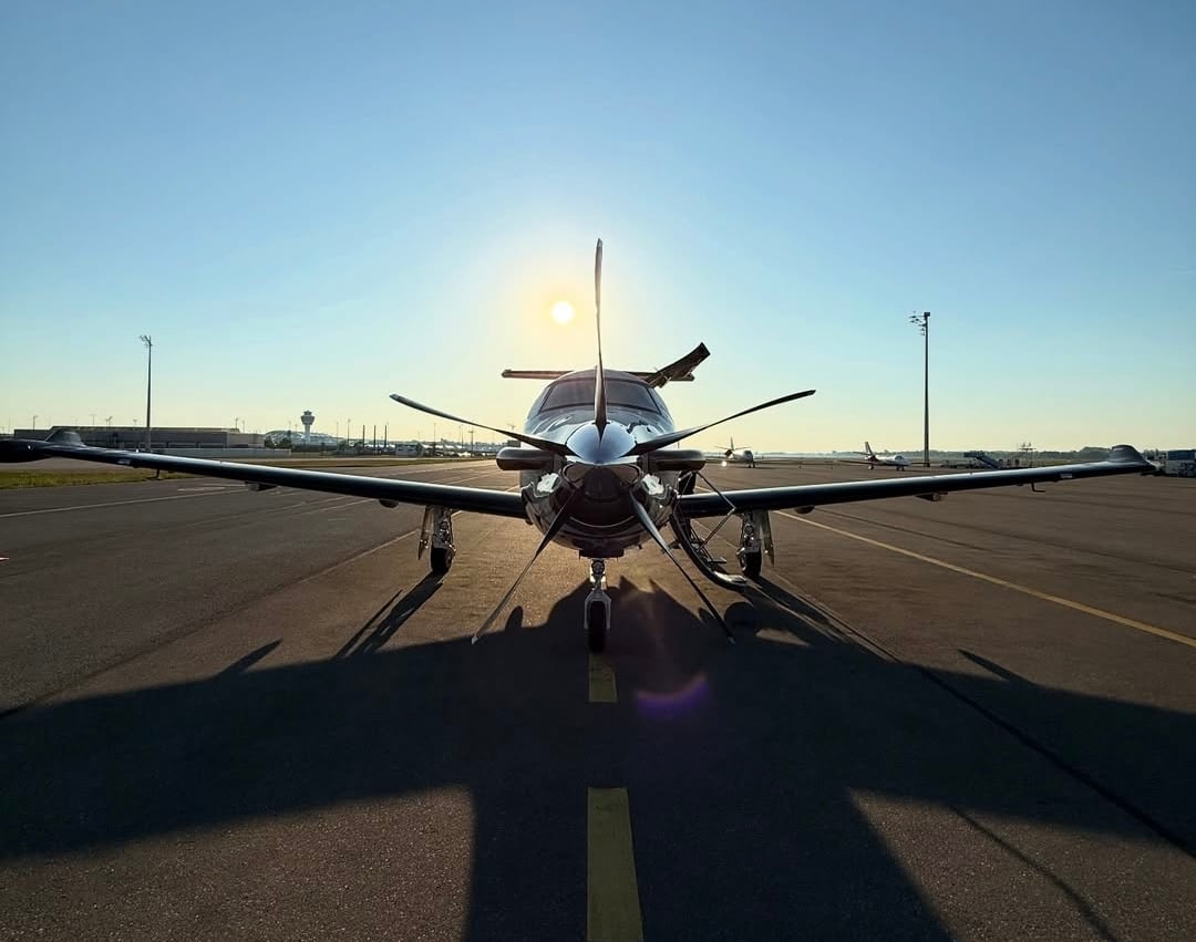 A white airplane flying over a body of water, viewed from above, showcasing its sleek design and single propeller.