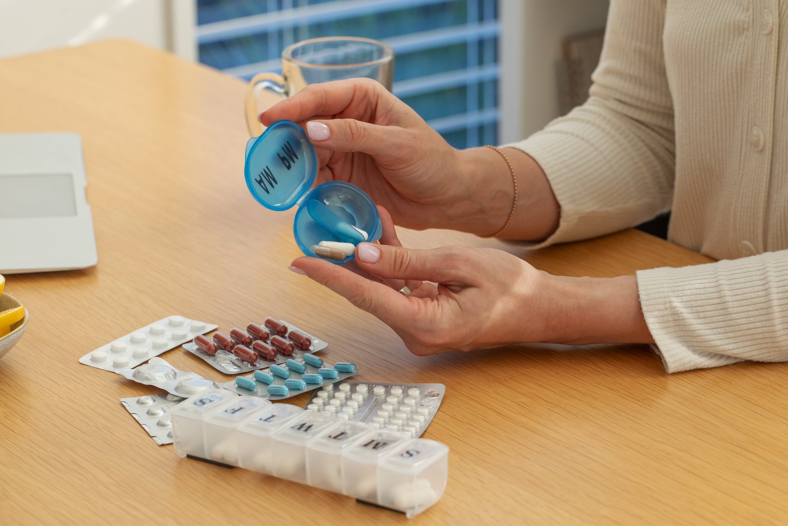 Daily medication organization with pill box and tablets on wooden table. Concept of health care