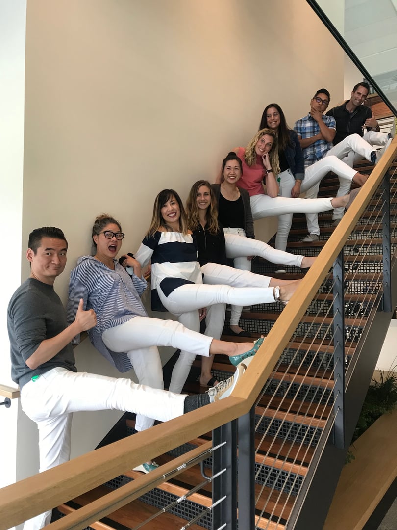 A group of people posing playfully on a staircase, all wearing white pants, with various expressions and gestures.