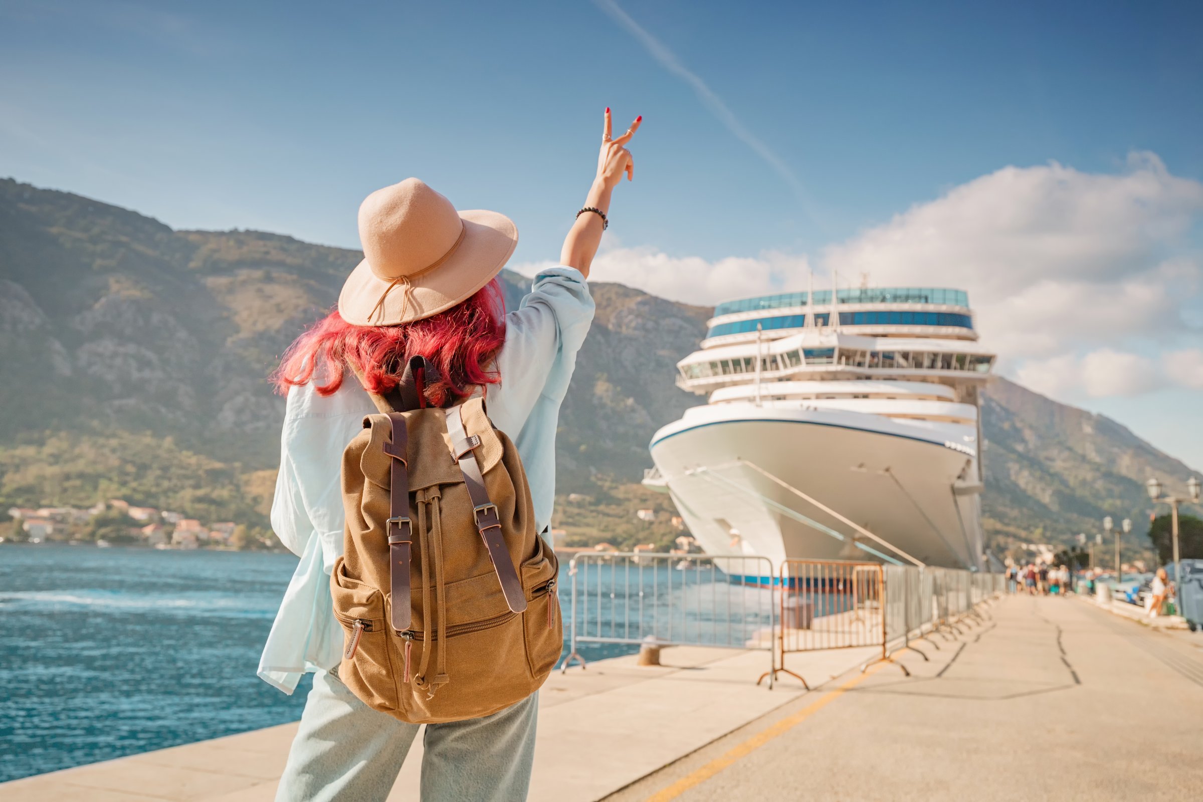 Tourist wearing backpack and hat gesturing near cruise ship at Kotor bay, Montenegro