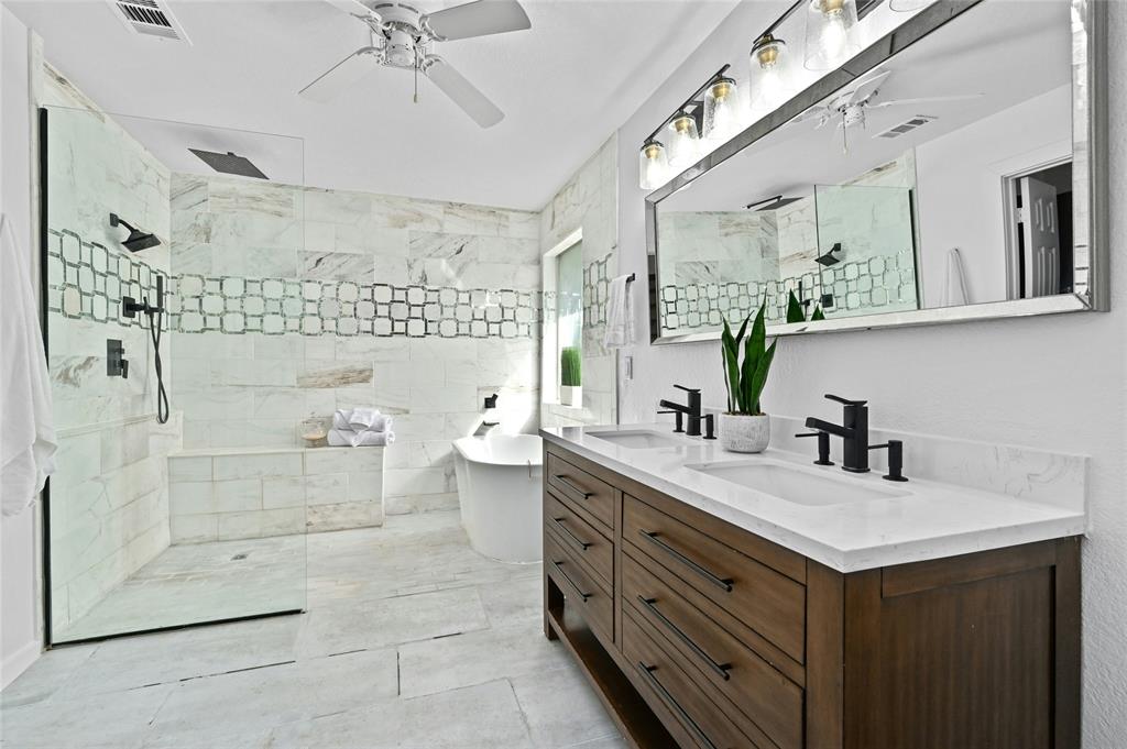 Modern bathroom with double sinks, large mirror, freestanding tub, walk-in shower, and white marble tiles.