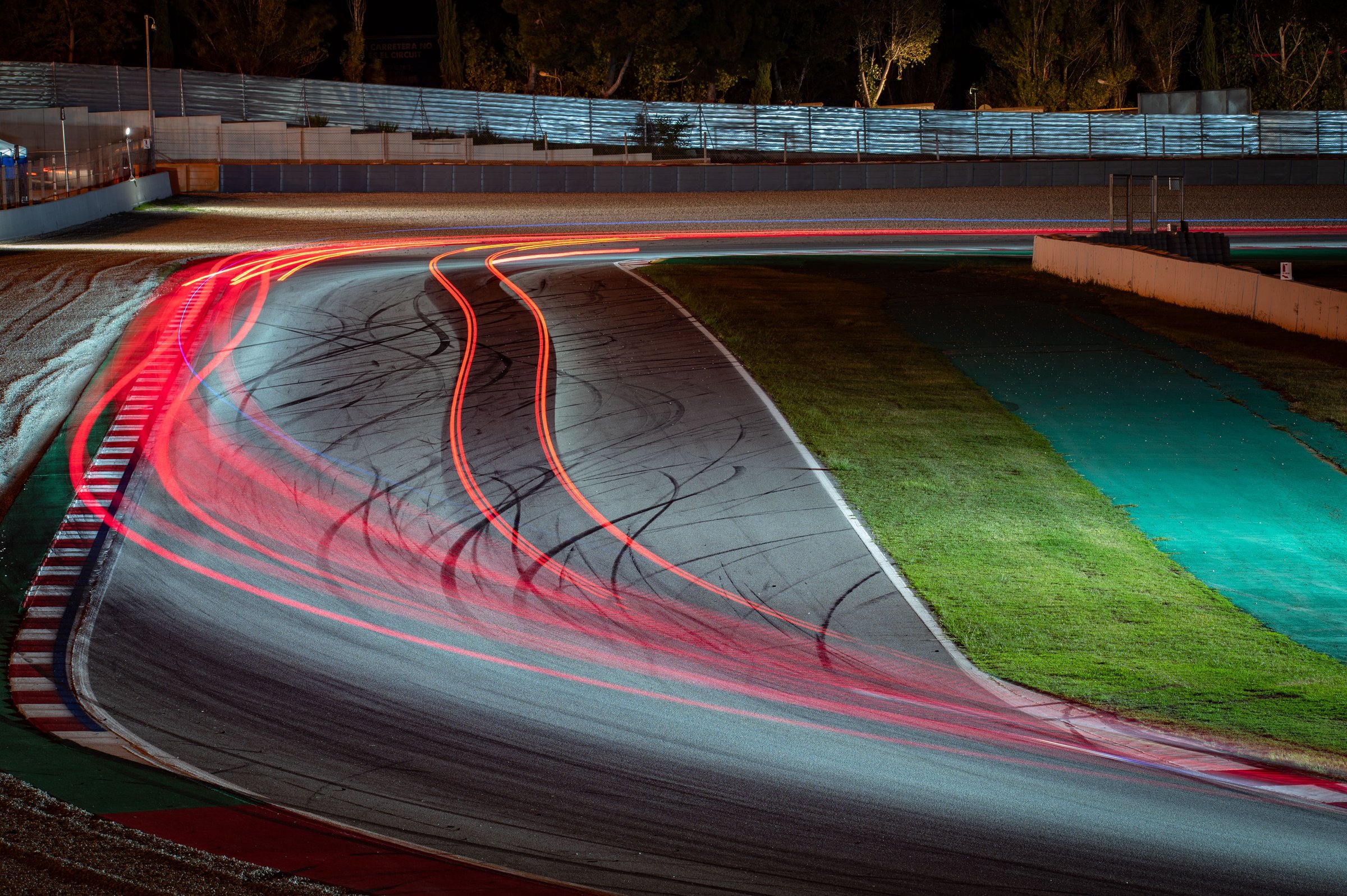 Long exposure night photography that shows the traces of light left by the racing cars as they pass through the curve.