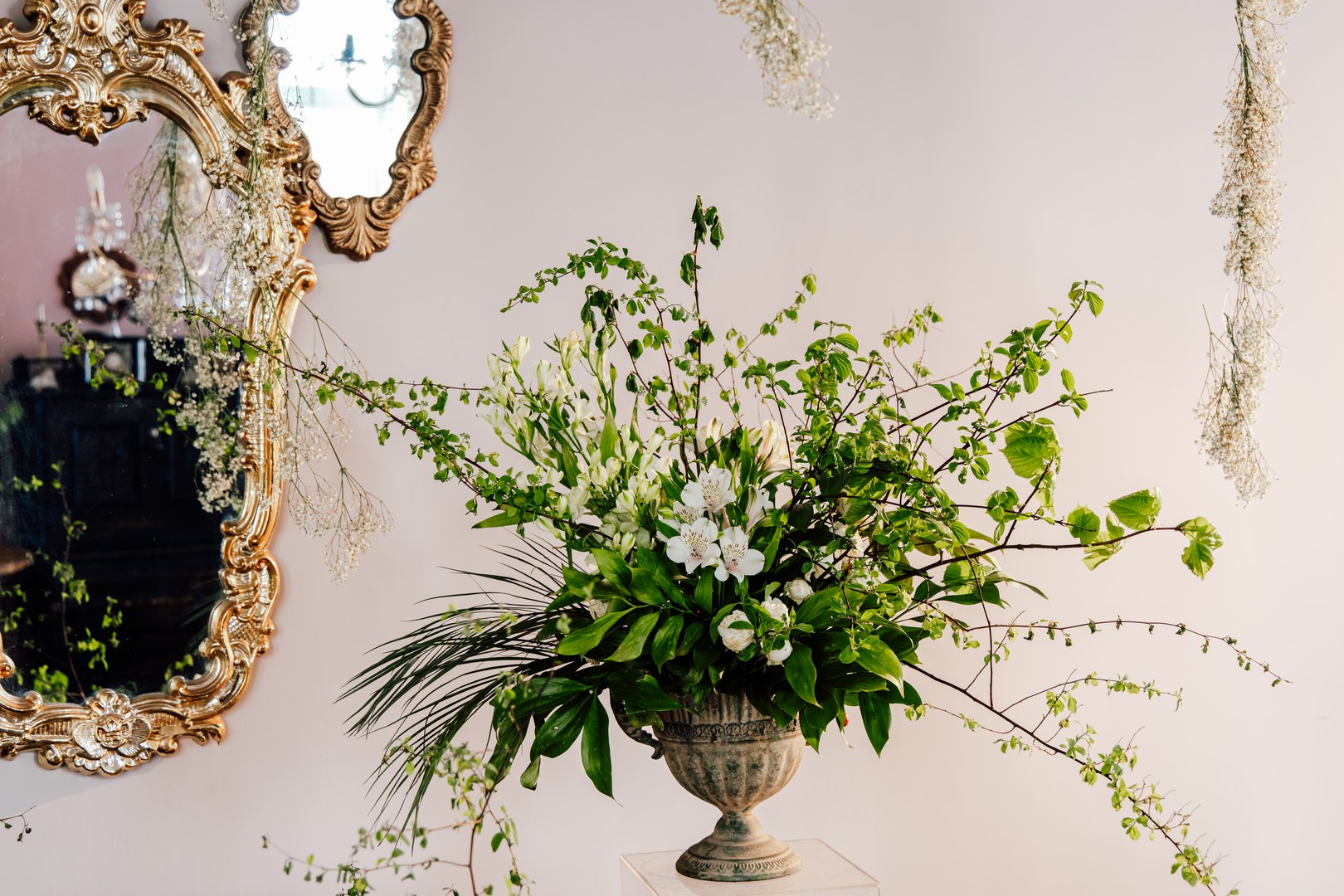 A beautiful floral display features white and green blooms in an ornate vintage vase. The arrangement complements the delicate decor with greenery and flowers adding freshness to the room.