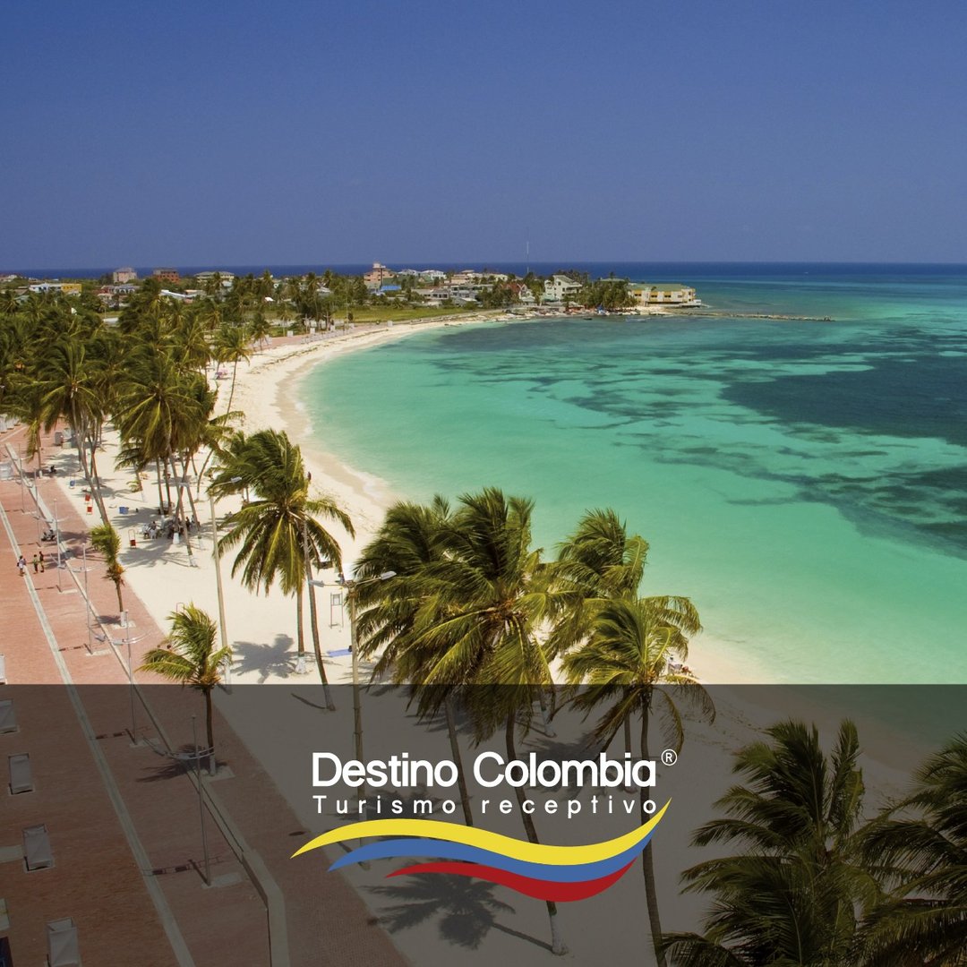 Aerial view of a tropical beach with turquoise water, palm trees, and a promenade in San Andrés, Colombia.