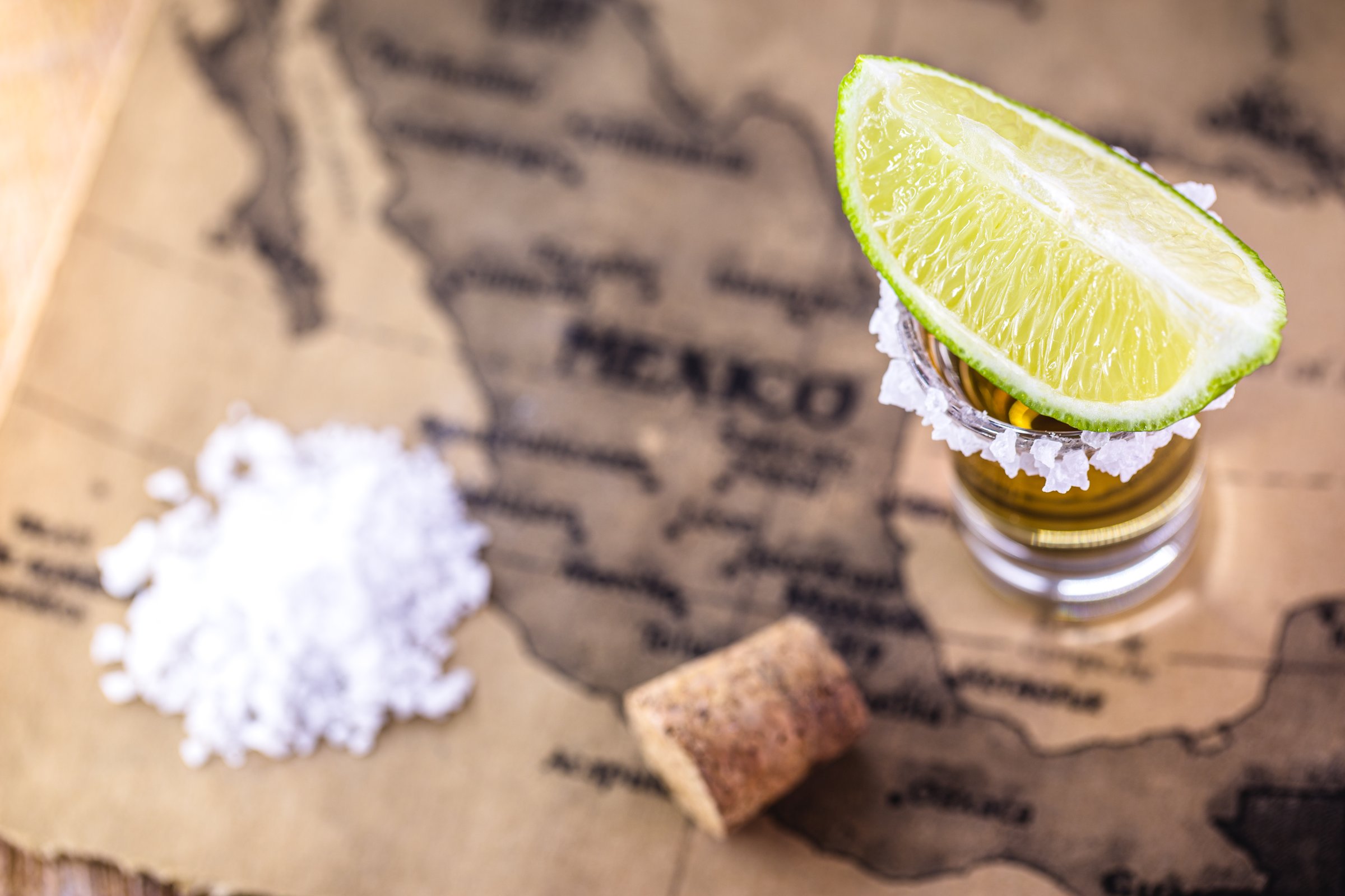 glasses of golden tequila, served with salt and lemon, over vintage map of mexico