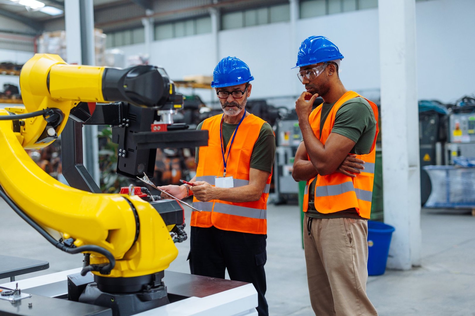 Two engineers analyzing a robotic arm in a factory setting, discussing its performance and potential improvements