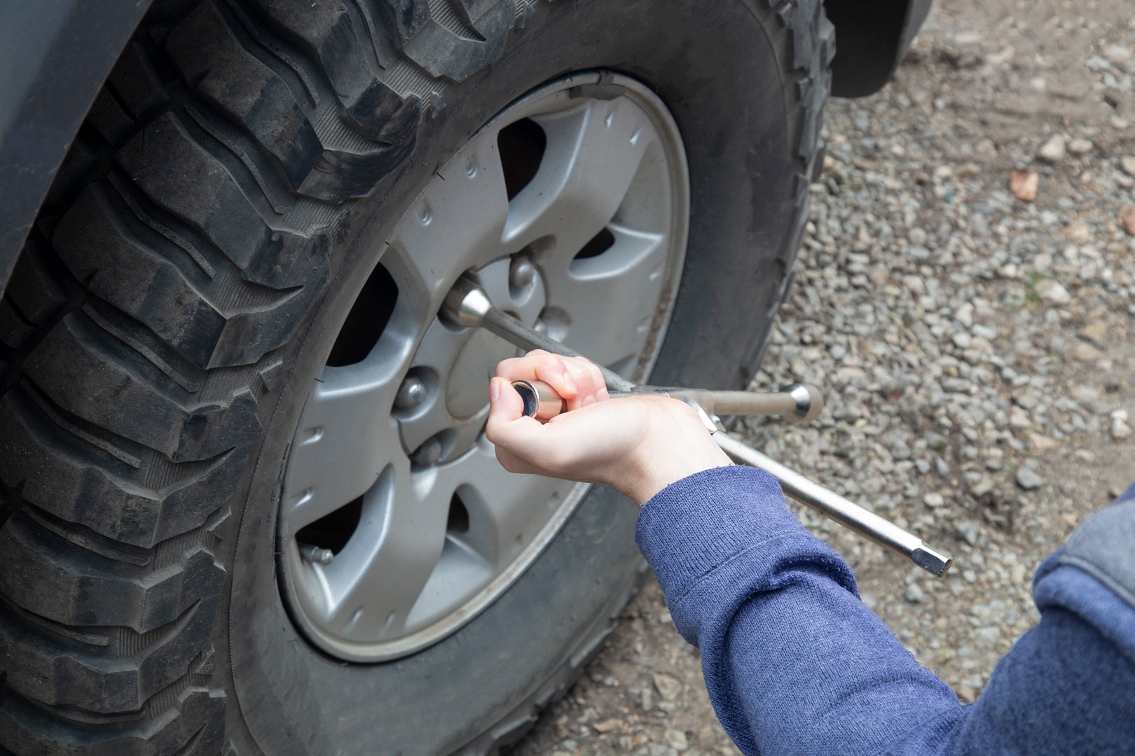 A man removes a wheel from a car using a wrench.