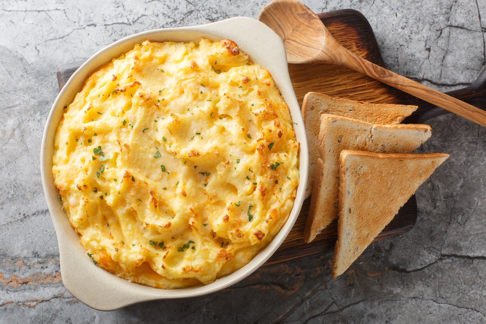 Golden baked mashed potatoes with cheddar and parmesan cheese, cream, butter and herbs close-up in a baking dish on the table. Horizontal top view from above
