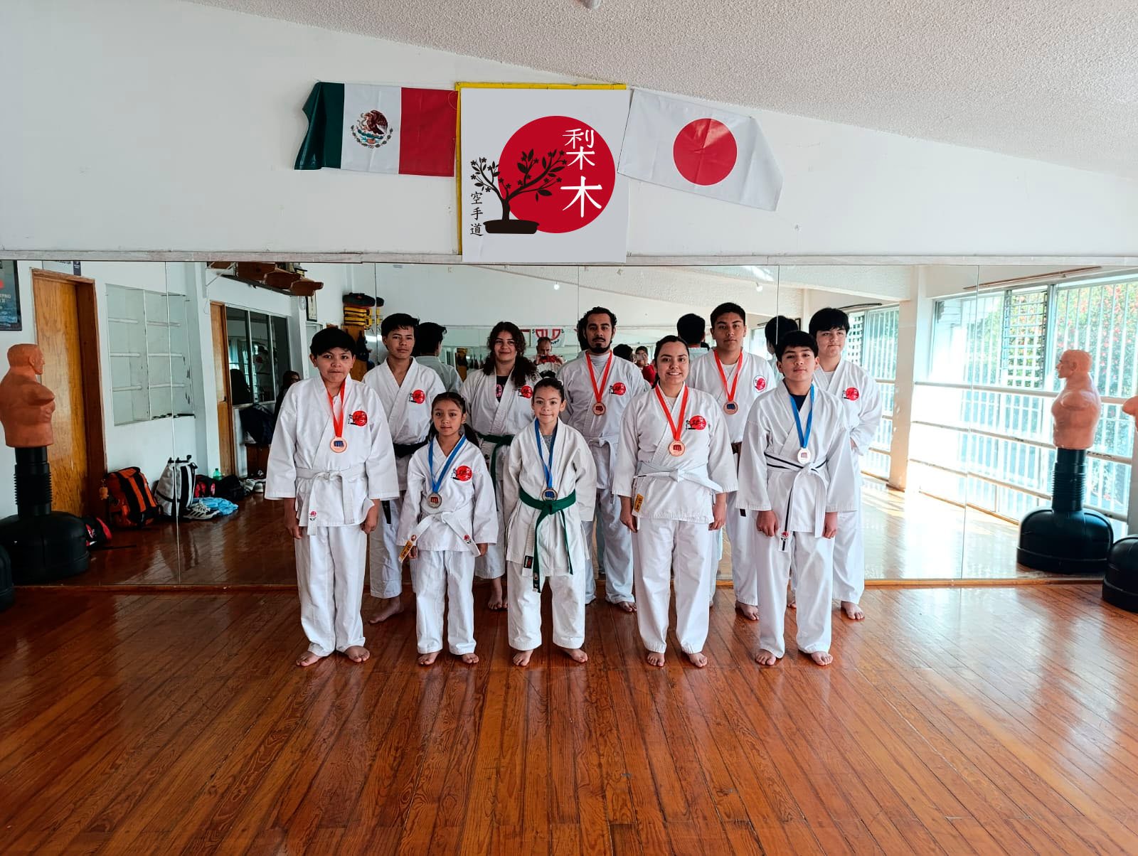 Karate class group photo with medals in a dojo, Mexican and Japanese flags in the background.