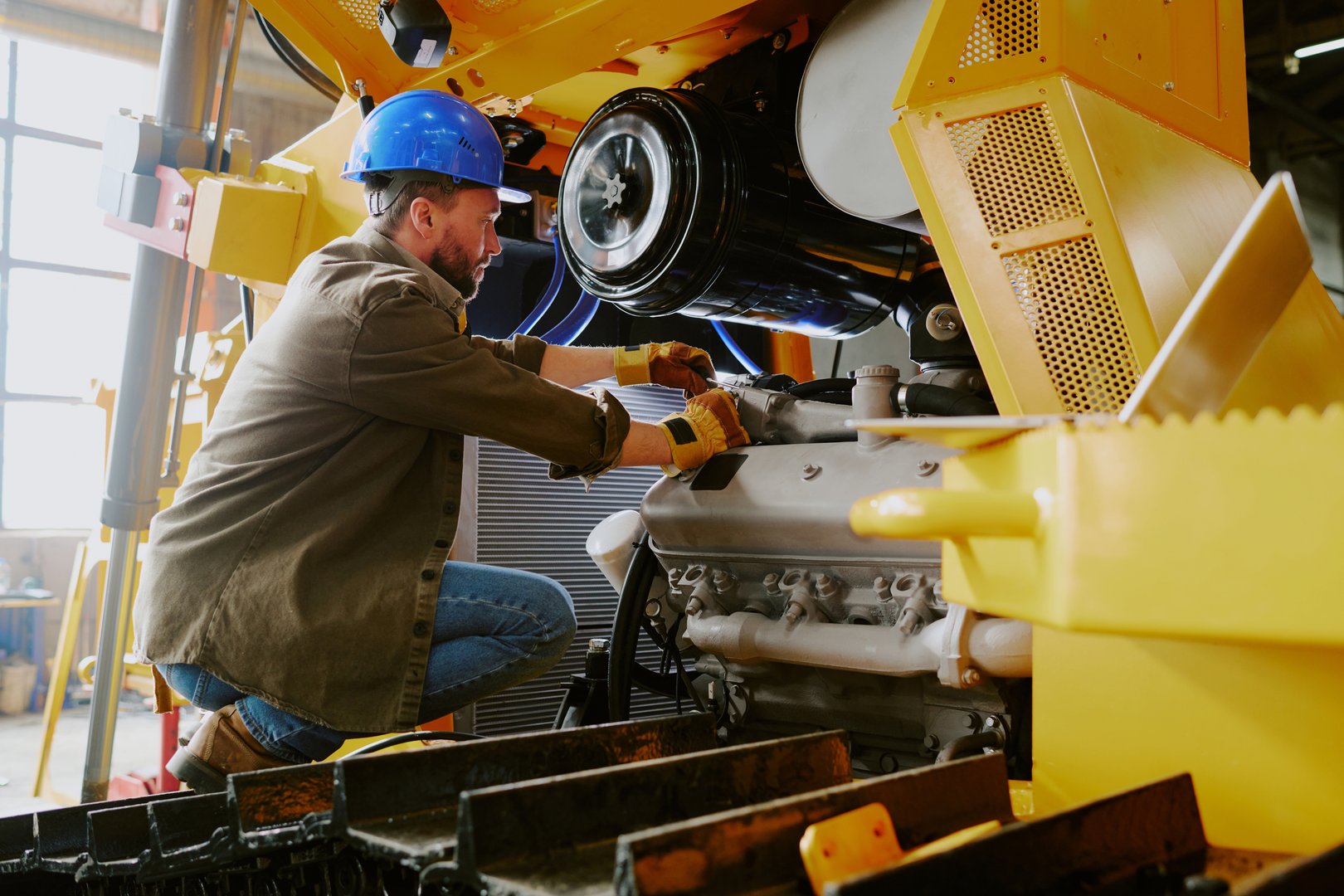 Caucasian male technician wearing hardhat maintaining new bulldozer at work in modern heavy machinery production plant