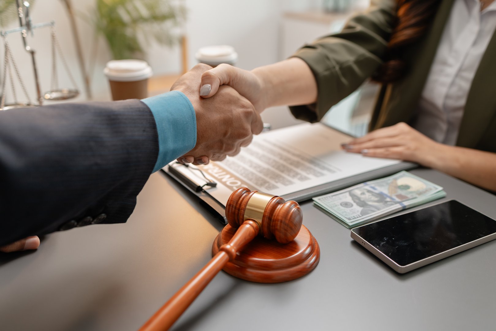 A business handshake between a lawyer and client after signing a contract in a modern office. The agreement document, gavel, and money on the table symbolize trust, legal success, and partnership.
