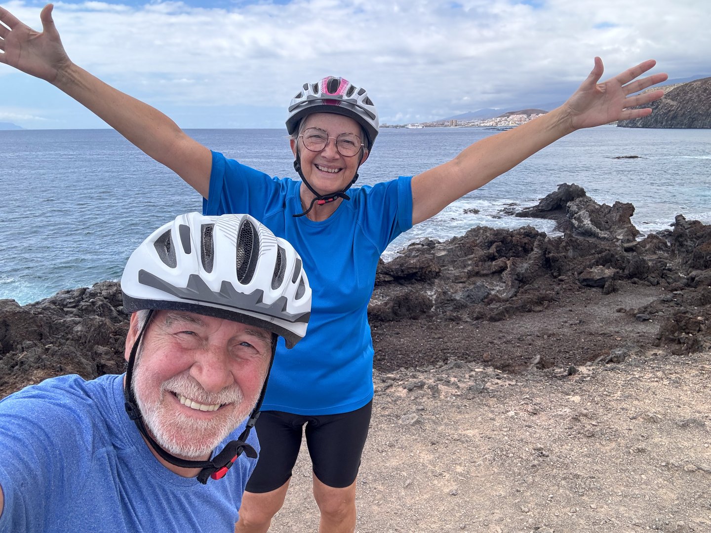 Happy joyful senior couple of cyclists in outdoor excursion at sea make a selfie laughing looking at camera. Two elderly retirees wearing helmet enjoy vacation and freedom