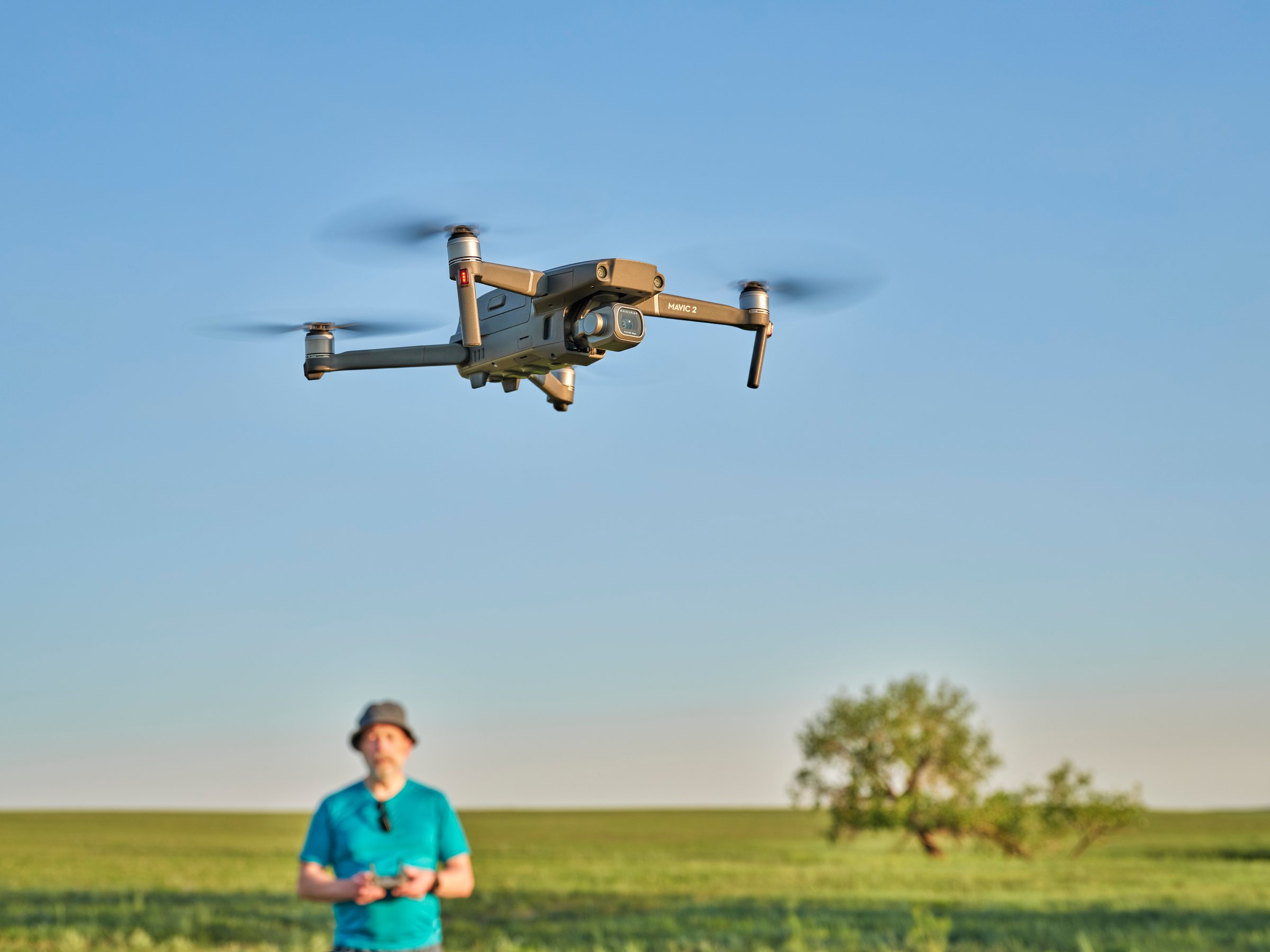 Briggsdale, CO, USA - June 8, 2021:  Radio controlled DJI Mavic 2 Pro quadcopter drone is flying over green prairie with a male pilot in background.