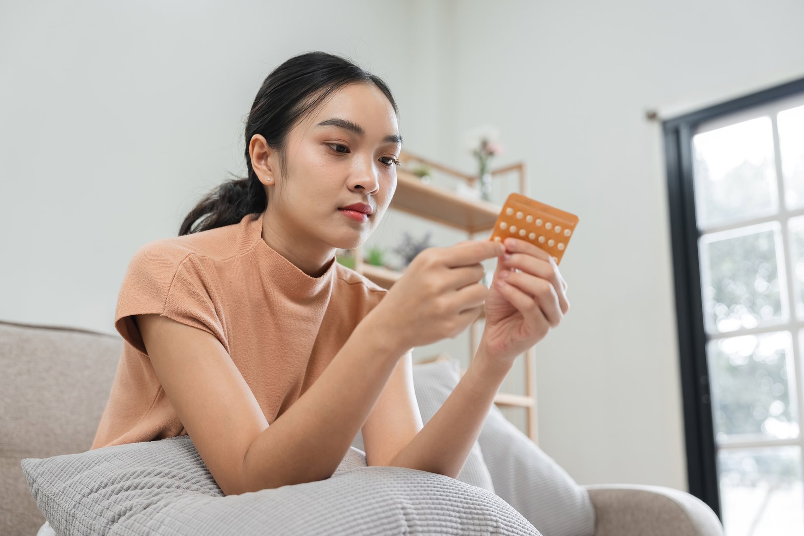 Young woman taking birth control pills, emphasizing contraceptive health, family planning, and modern healthcare in a home setting.