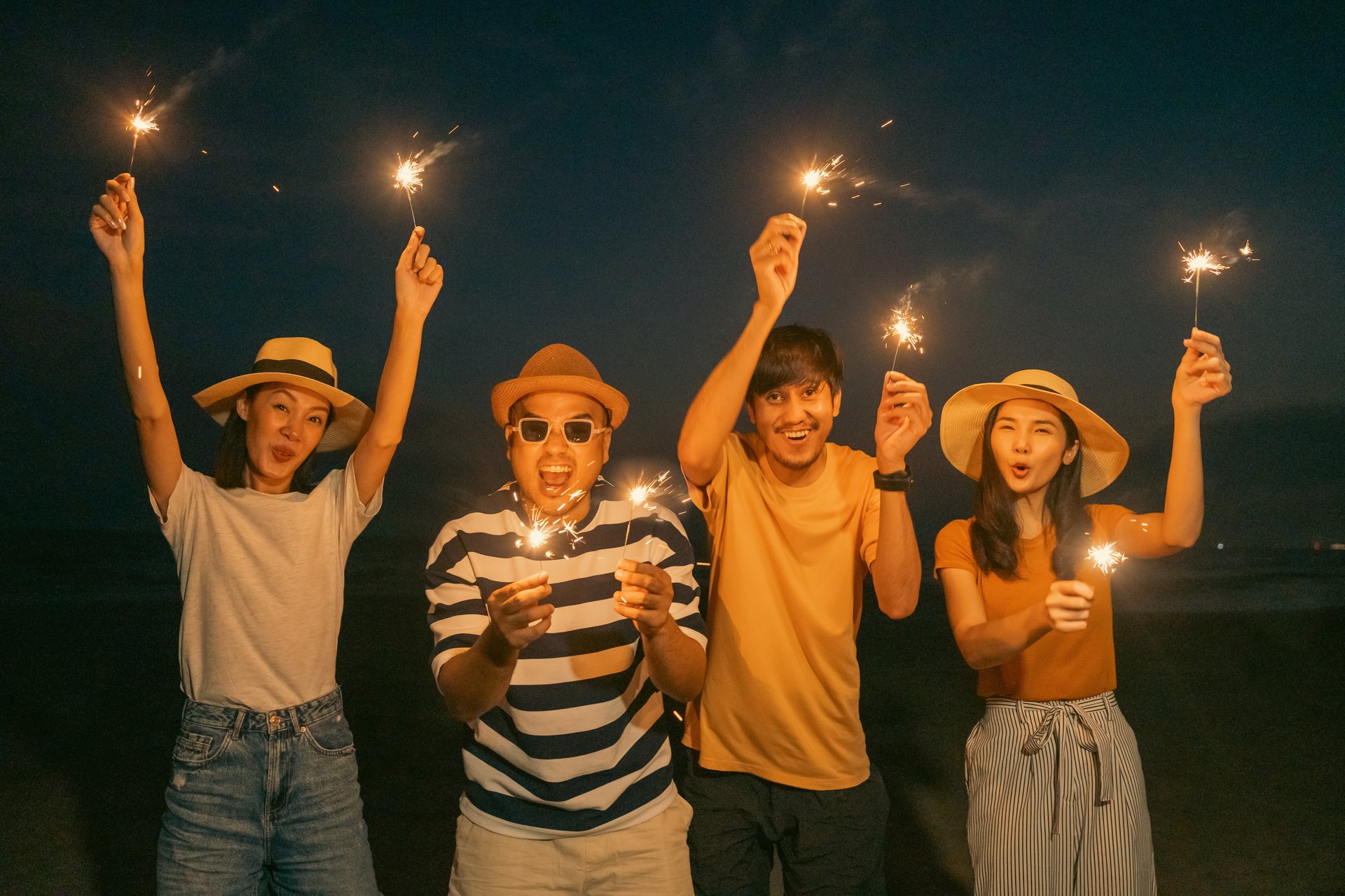 Happy friends cheering with fireworks at beach party outdoor. People vacation holiday on beach. Summer holiday having fun relax vacation time in the evening