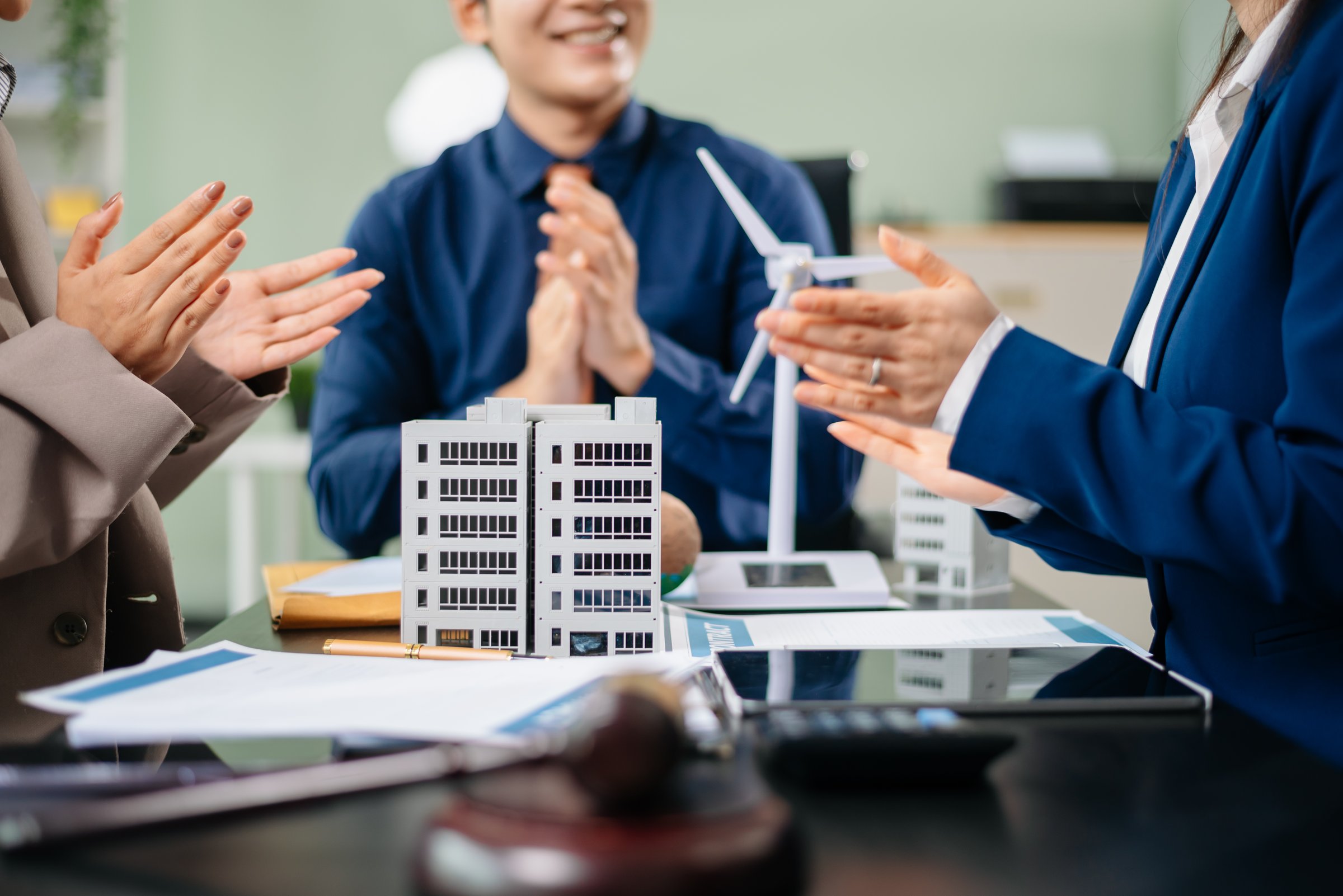 Group of professionals brainstorming with wind turbine and city model for sustainable energy project. Perfect for eco innovation, teamwork, and environmental solutions.
