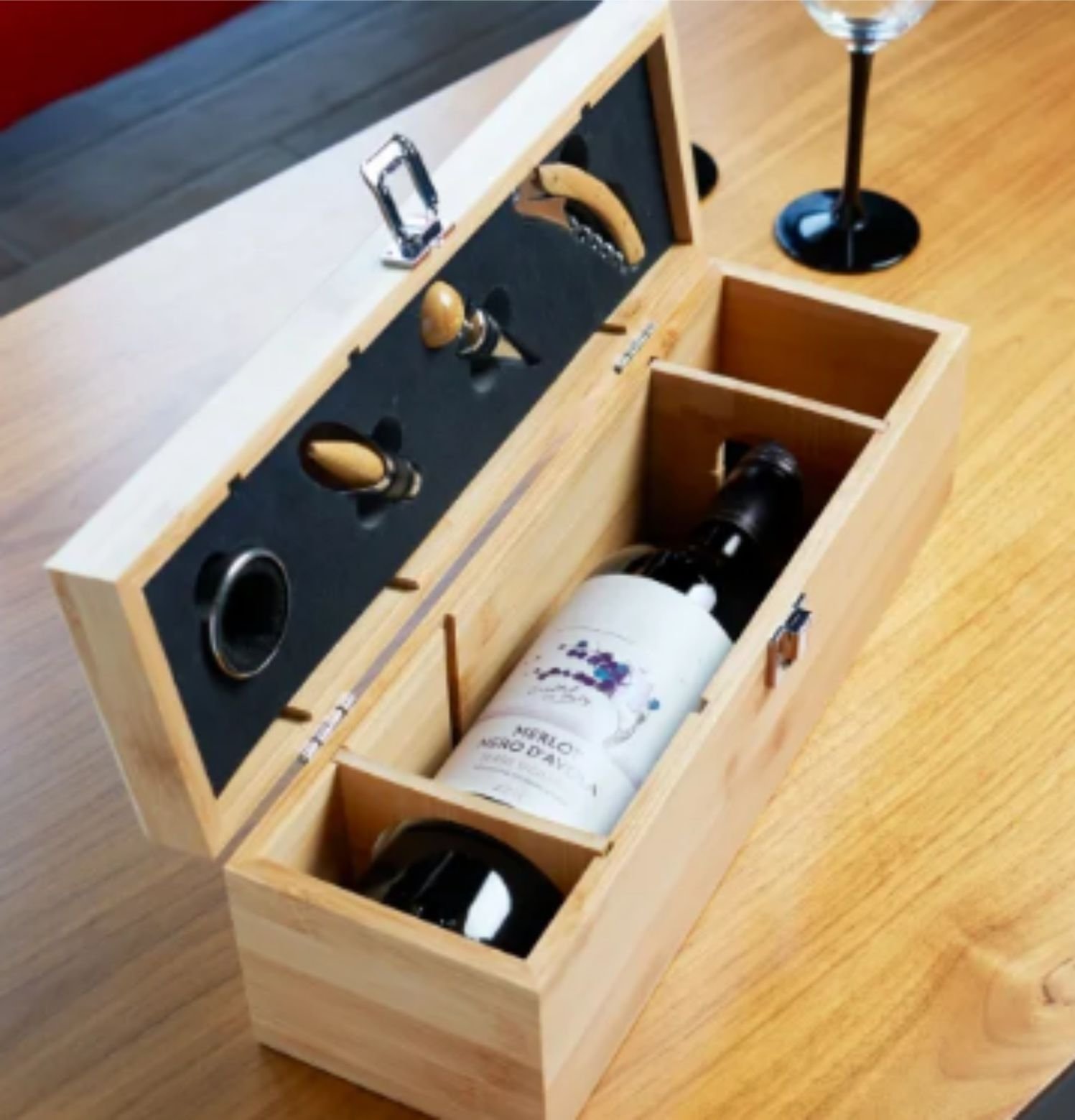 Wooden wine gift box with a bottle inside, includes corkscrew and stopper, displayed on a table.