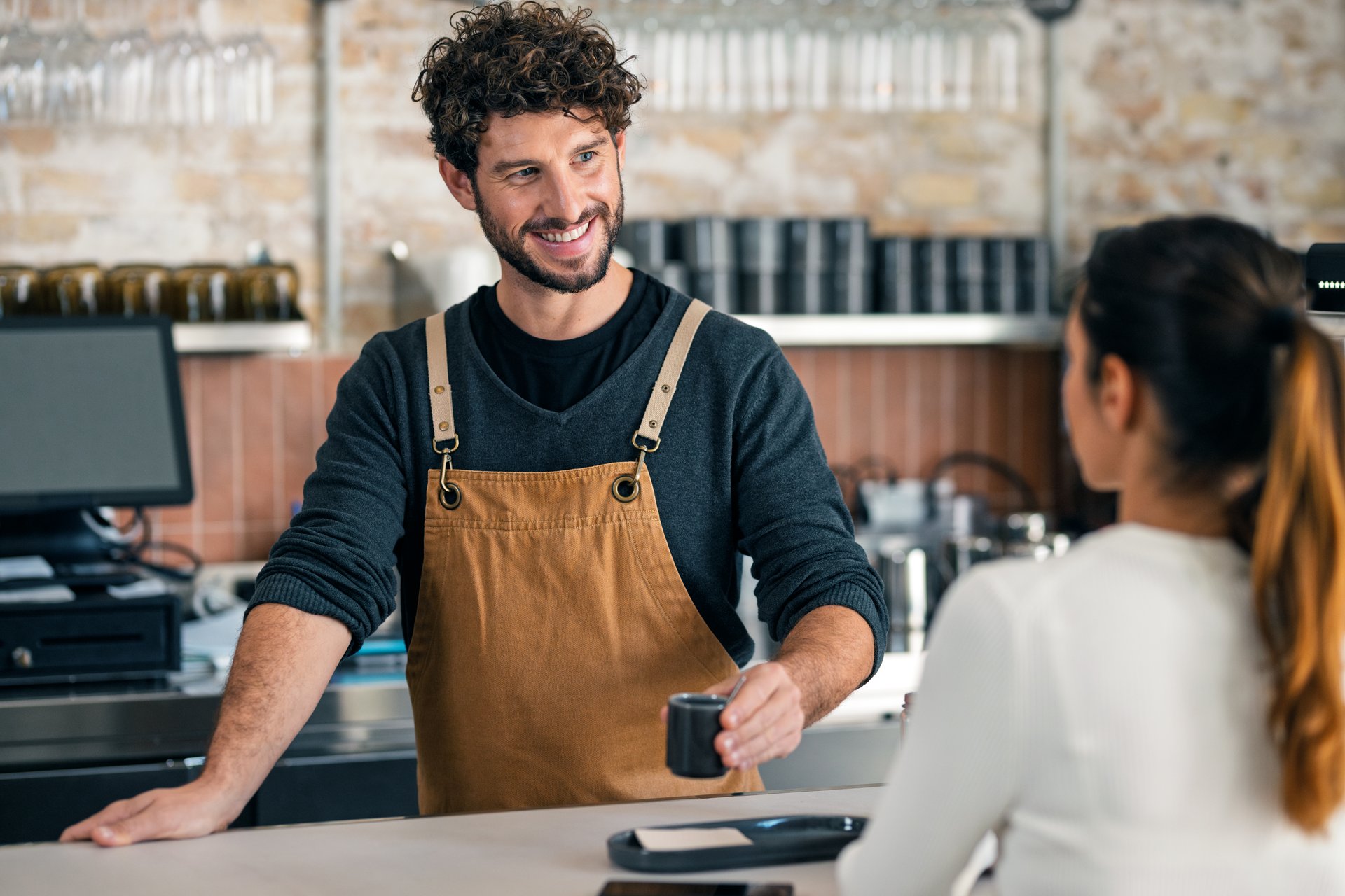 Shot of a handsome waiter talking with a client while serving a cup of coffee in the pastry shop