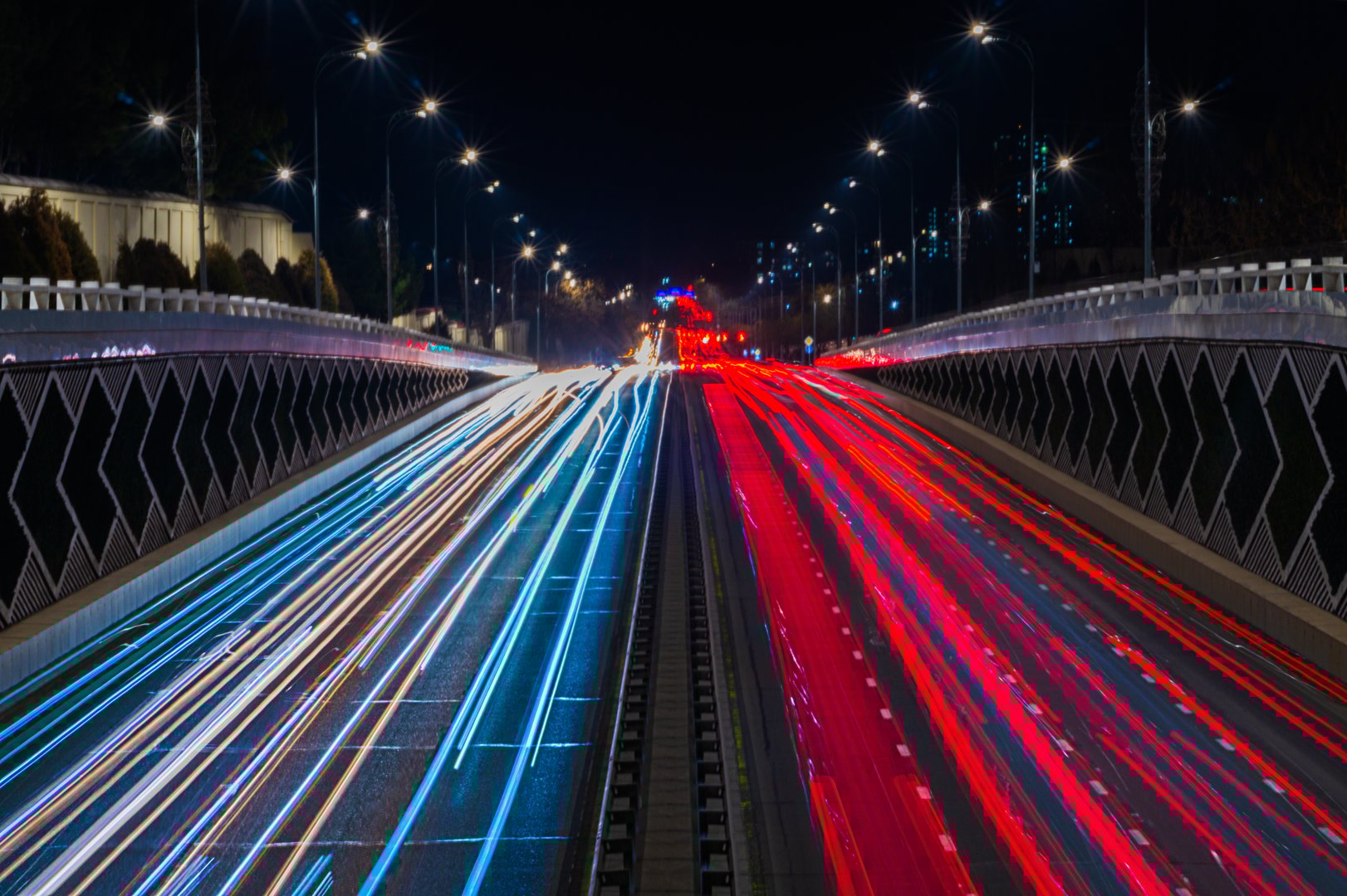 An eight-lane highway at night, illuminated by street lamps. The photo was taken with a long exposure, in which the movement of cars leaves light trails of yellow, blue, red.