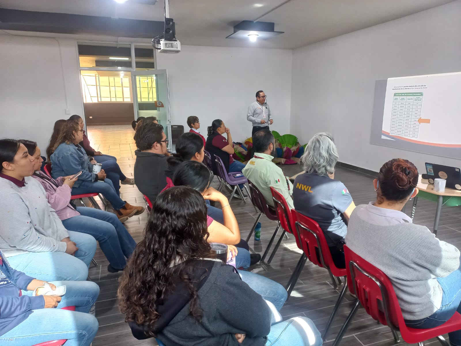 People seated in a classroom attentively listening to a presentation projected on a screen.