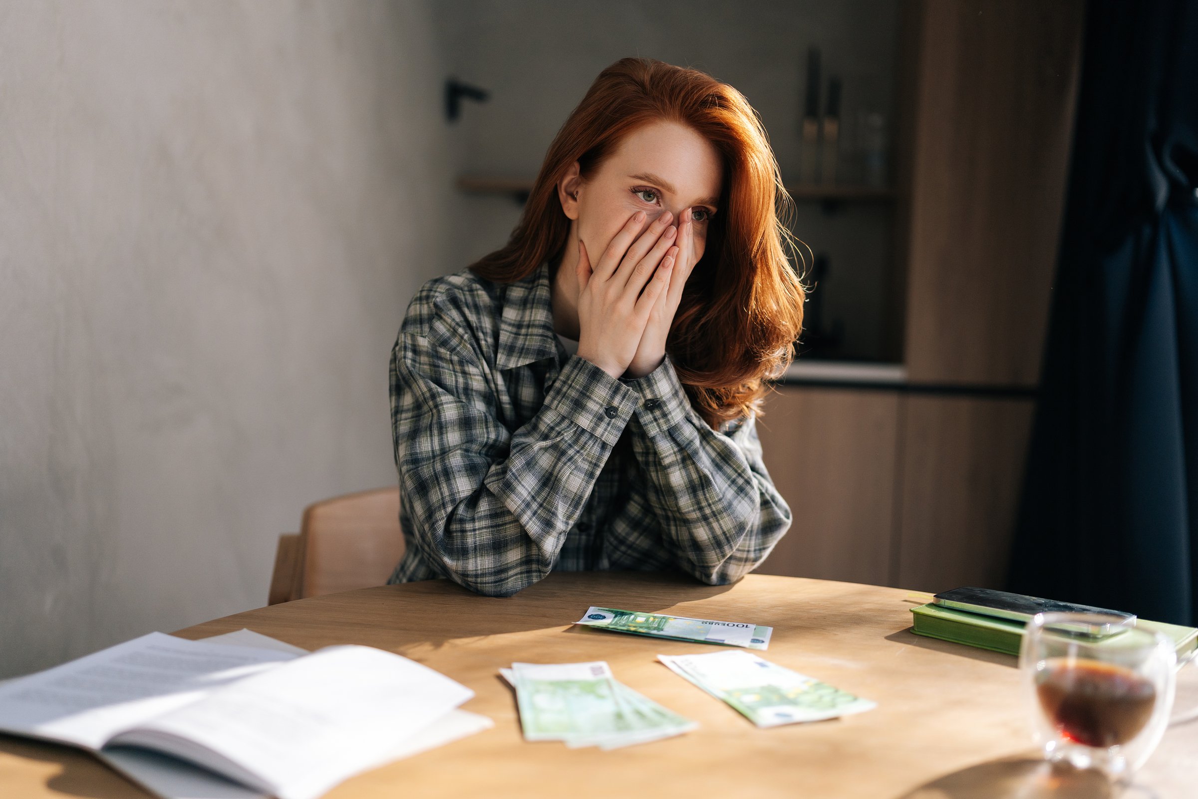 Desperate young woman counting money with sad expression, sitting at home kitchen table. Sad female having financial literacy and loan repayment. Concept of financial crisis.