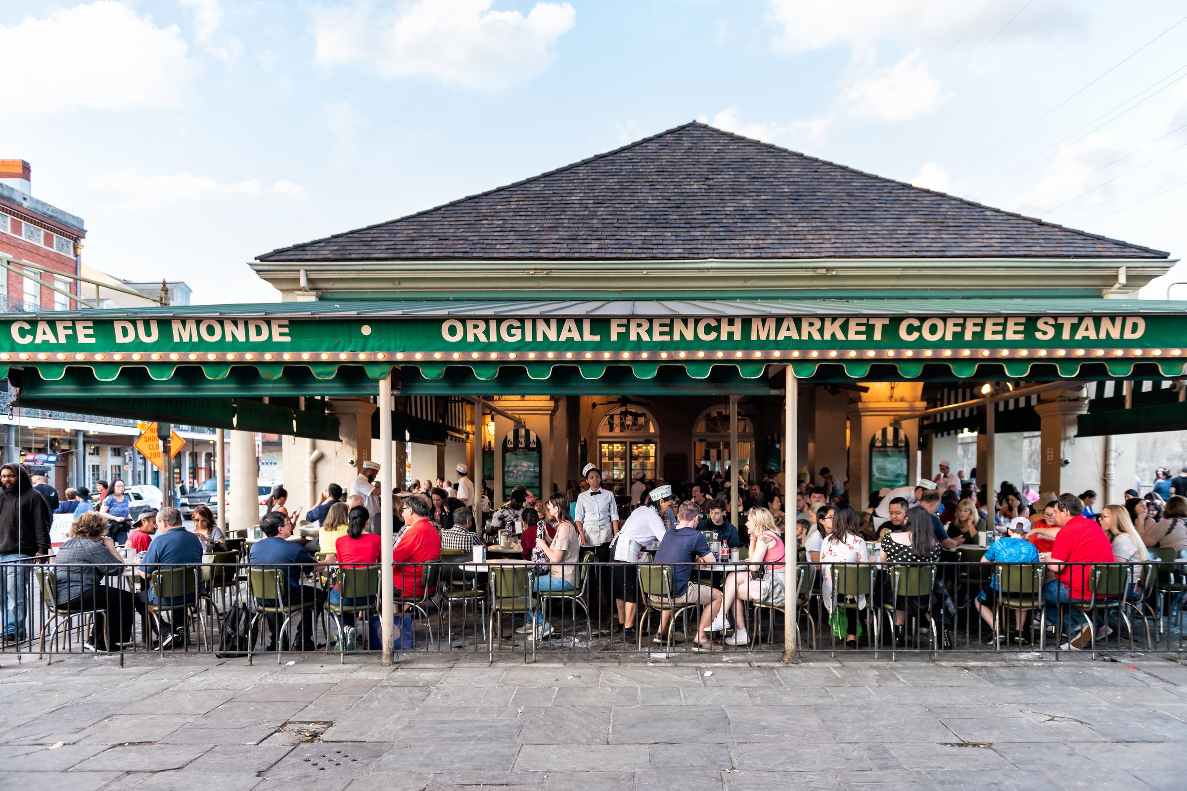 New Orleans, USA - April 22, 2018: People sitting at tables at iconic Cafe Du Monde restaurant sign eating beignet powdered sugar donuts and chicory coffee
