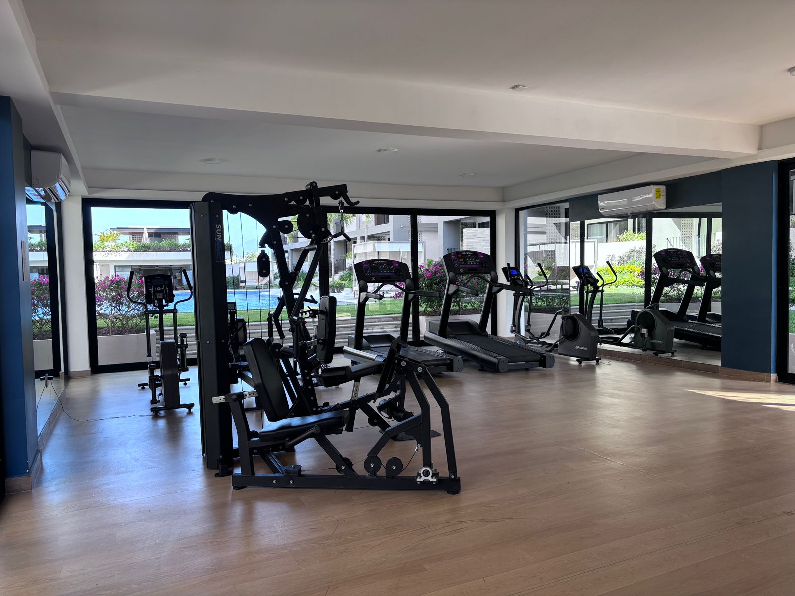 Modern gym with exercise machines, including treadmills and weight equipment, in a spacious room with large windows.