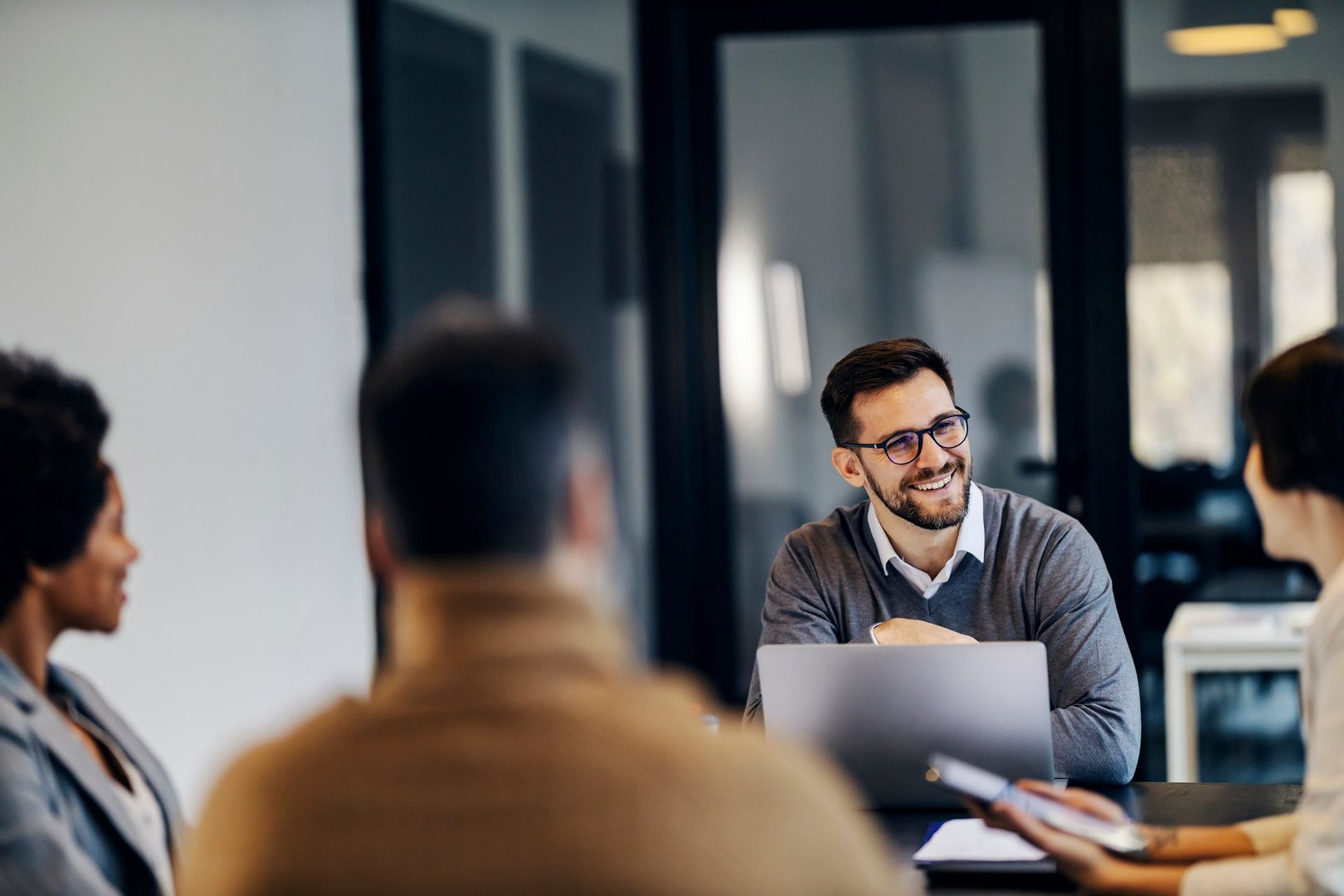 A happy manager is sitting in the co working space with colleagues and having business meeting.