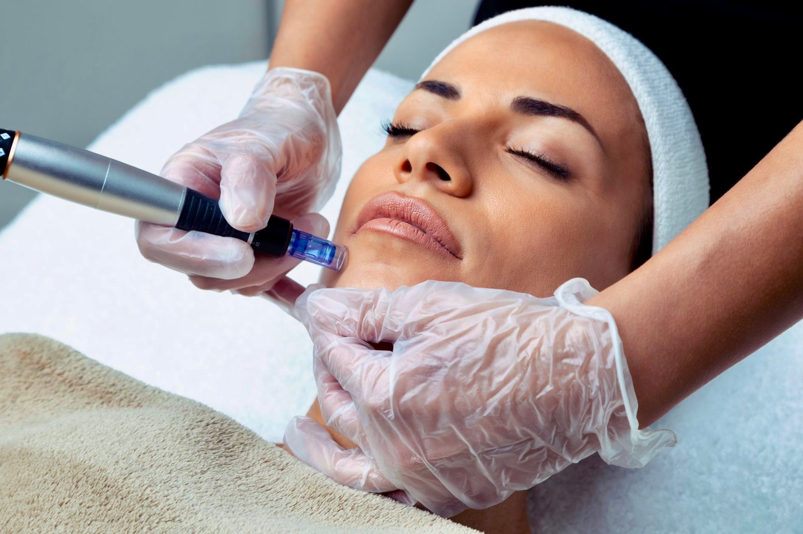 Person receiving a skin treatment with a dermapen by a professional wearing gloves. The person has their eyes closed.