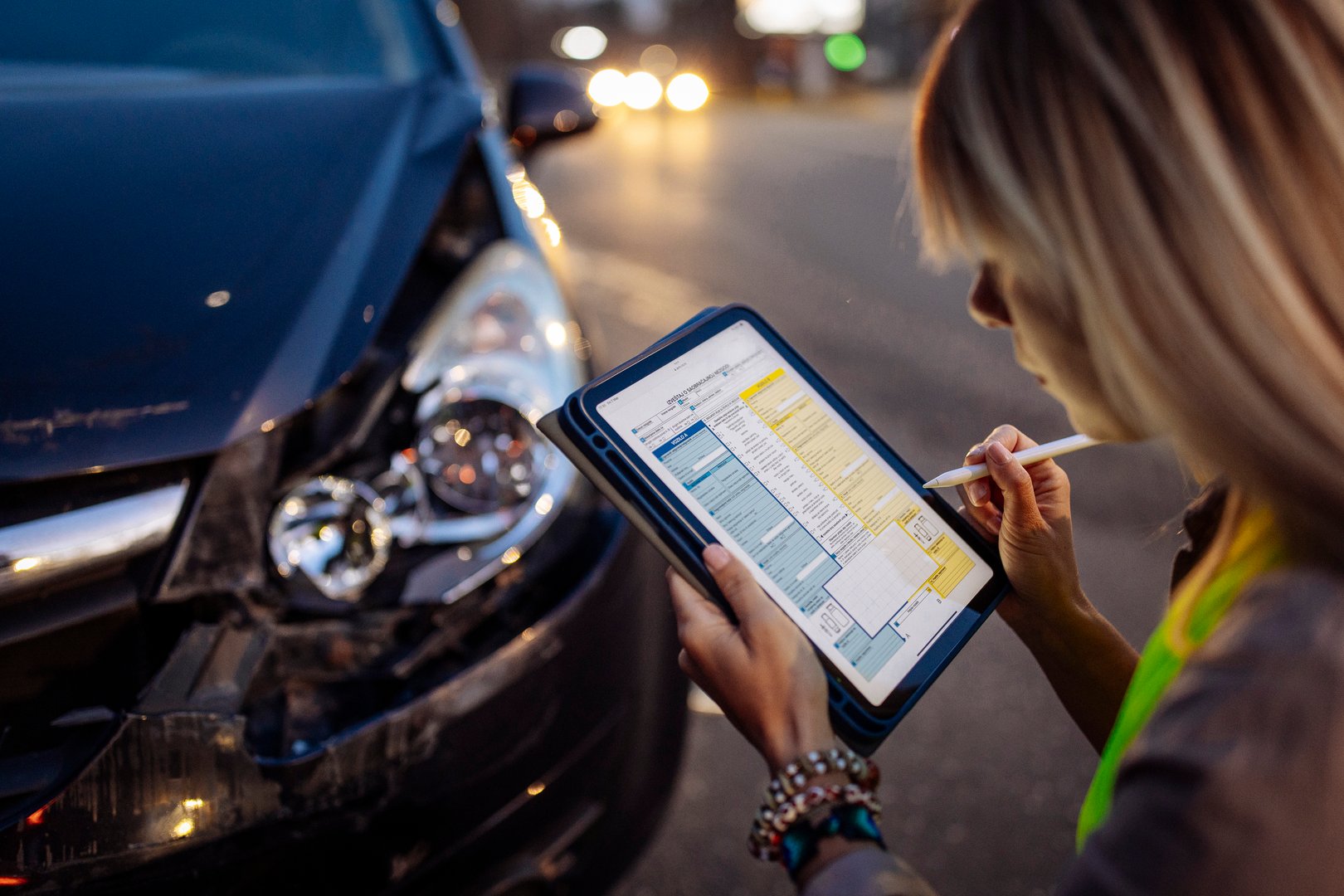 Young woman wearing a reflective safety vest writes on a clipboard or digital tablet near a damaged car after a traffic accident. She appears focused and calm while documenting the incident. This image is ideal for illustrating car insurance claims, roadside assistance, responsible driving, and post-accident procedures.