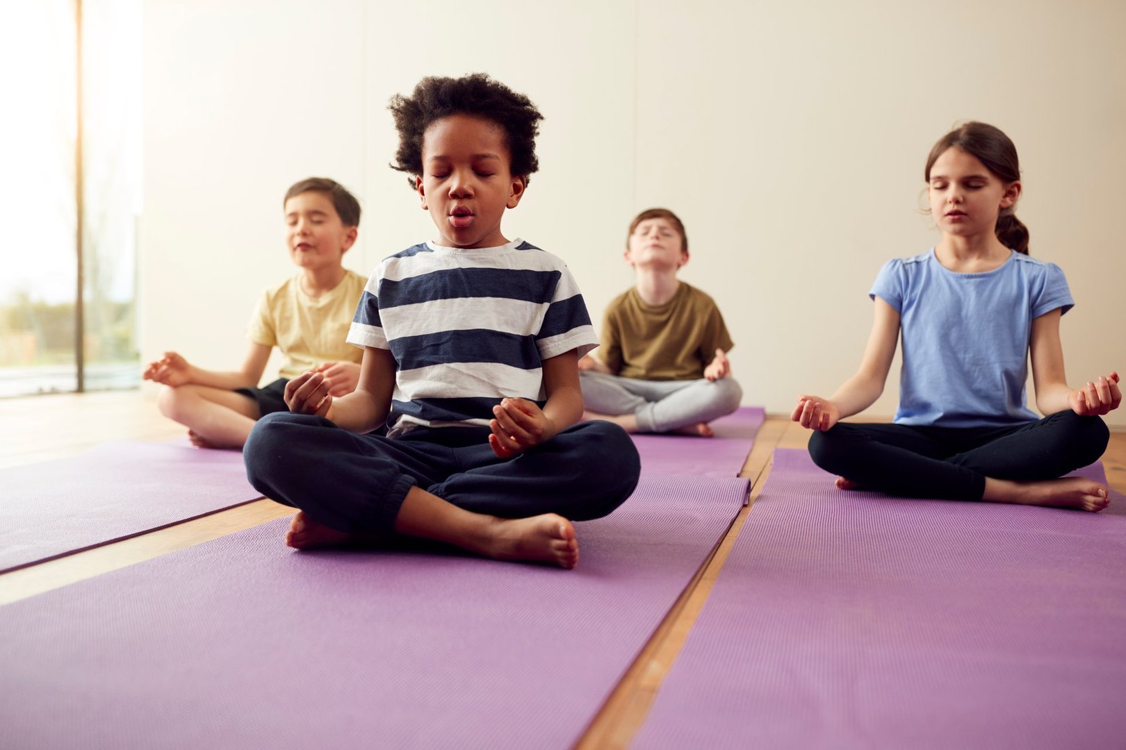 Group Of Children Sitting On Exercise Mats And Meditating In Yoga Studio