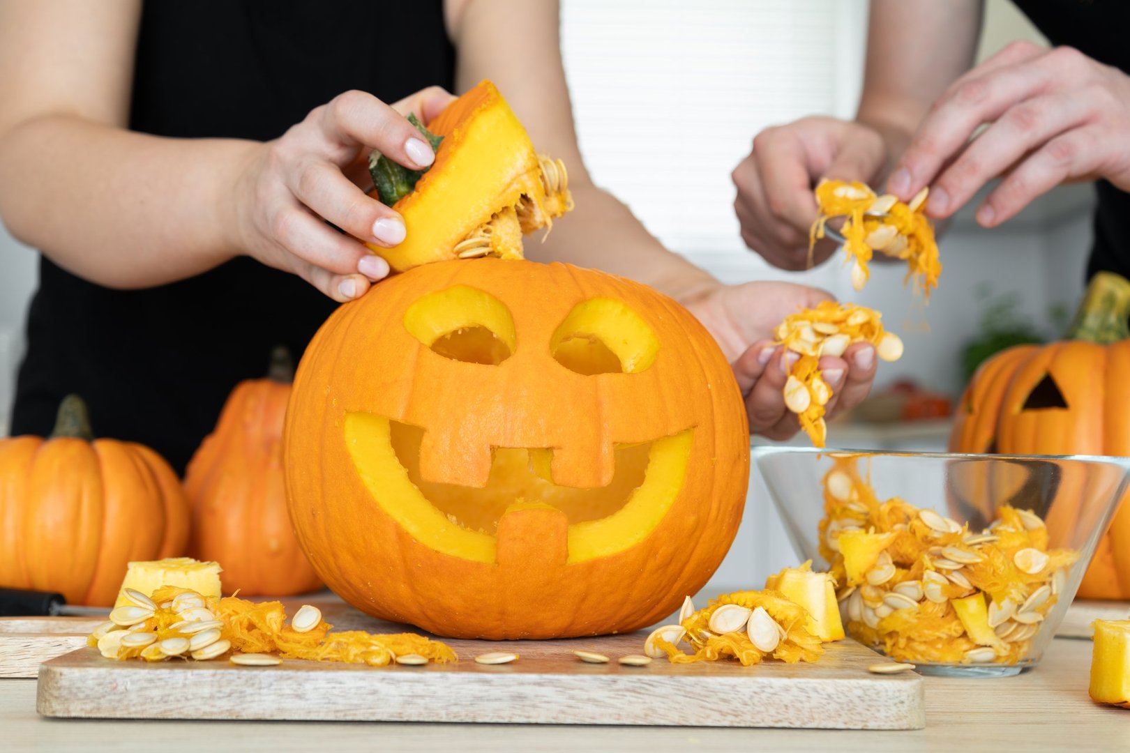Man and woman hands gutting Halloween pumpkin. Couple of people hollowing Jack-o'-lantern, removing guts and seeds from a Halloween pumpkin by reaching inside through the cut-off top lid.