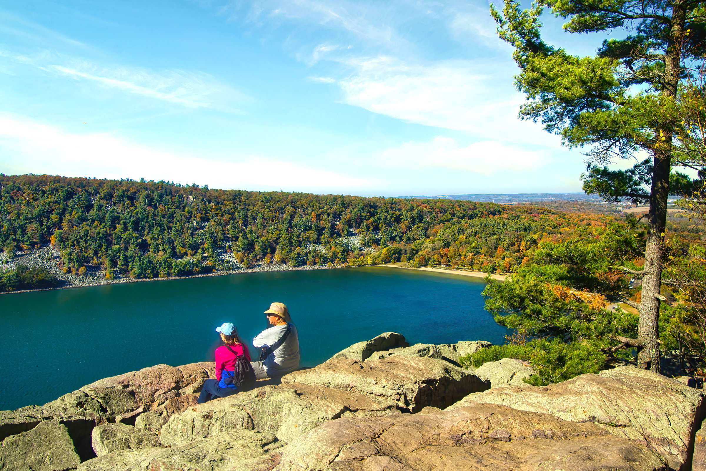 Sunny Autumn landscape featuring two adults sitting on a rocky cliff admiring the high altitude view at Devil's Lake State Park near Baraboo, Wisconsin.