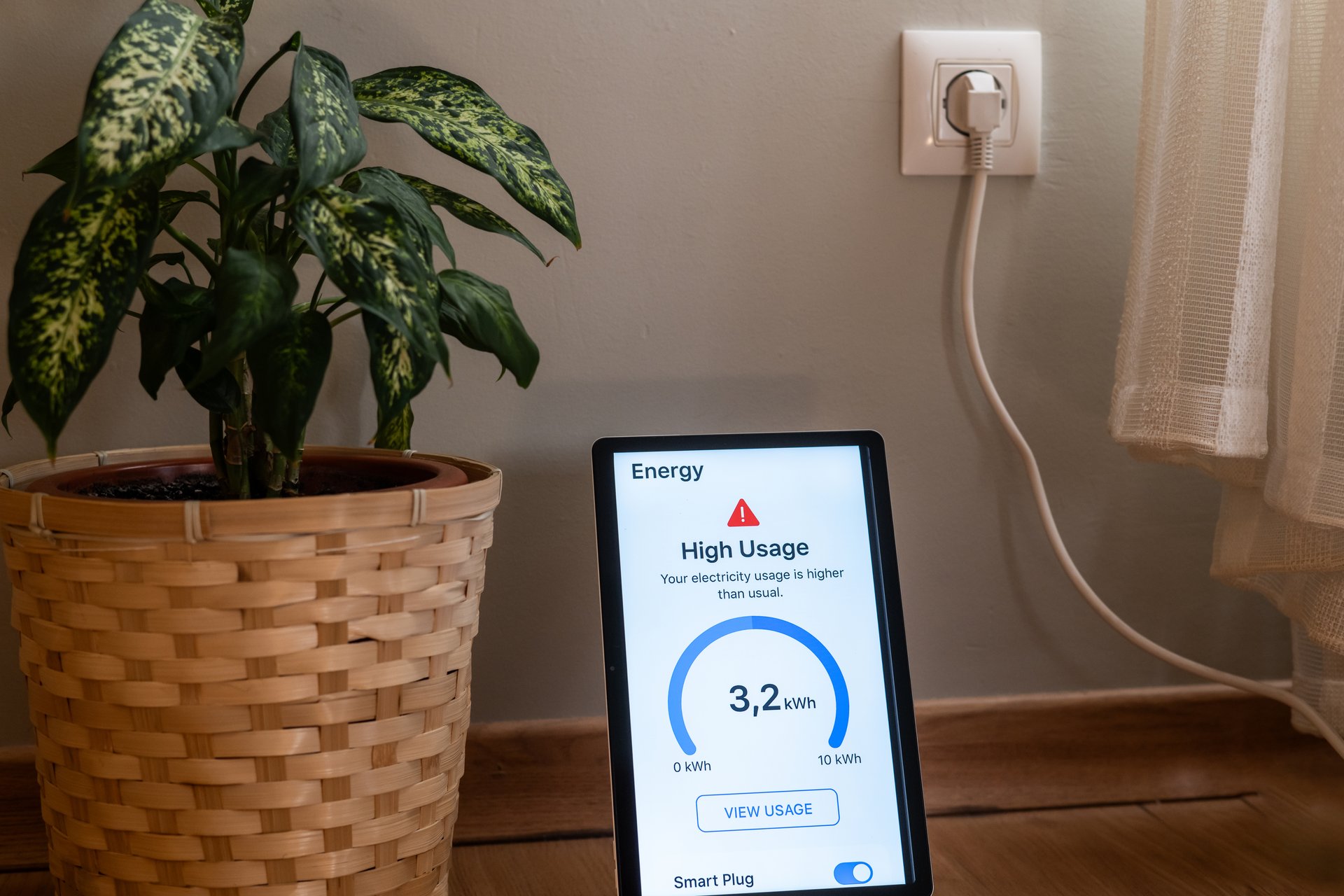 Tablet displaying a high electricity usage alert from a smart plug, indicating excessive energy consumption in a home setting, with a plant in a wicker basket nearby