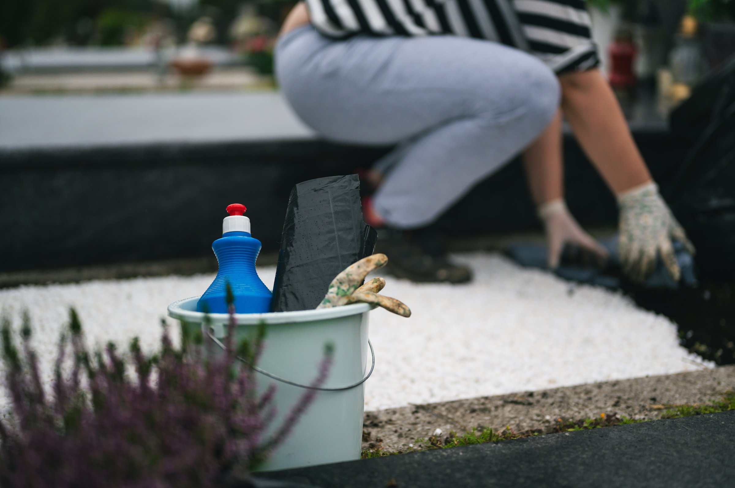 Cemetery autumn maintenance work  before the All Saints Day. Various cleaning tool in focus with unrecognizable person taking care of grave in blurred background.