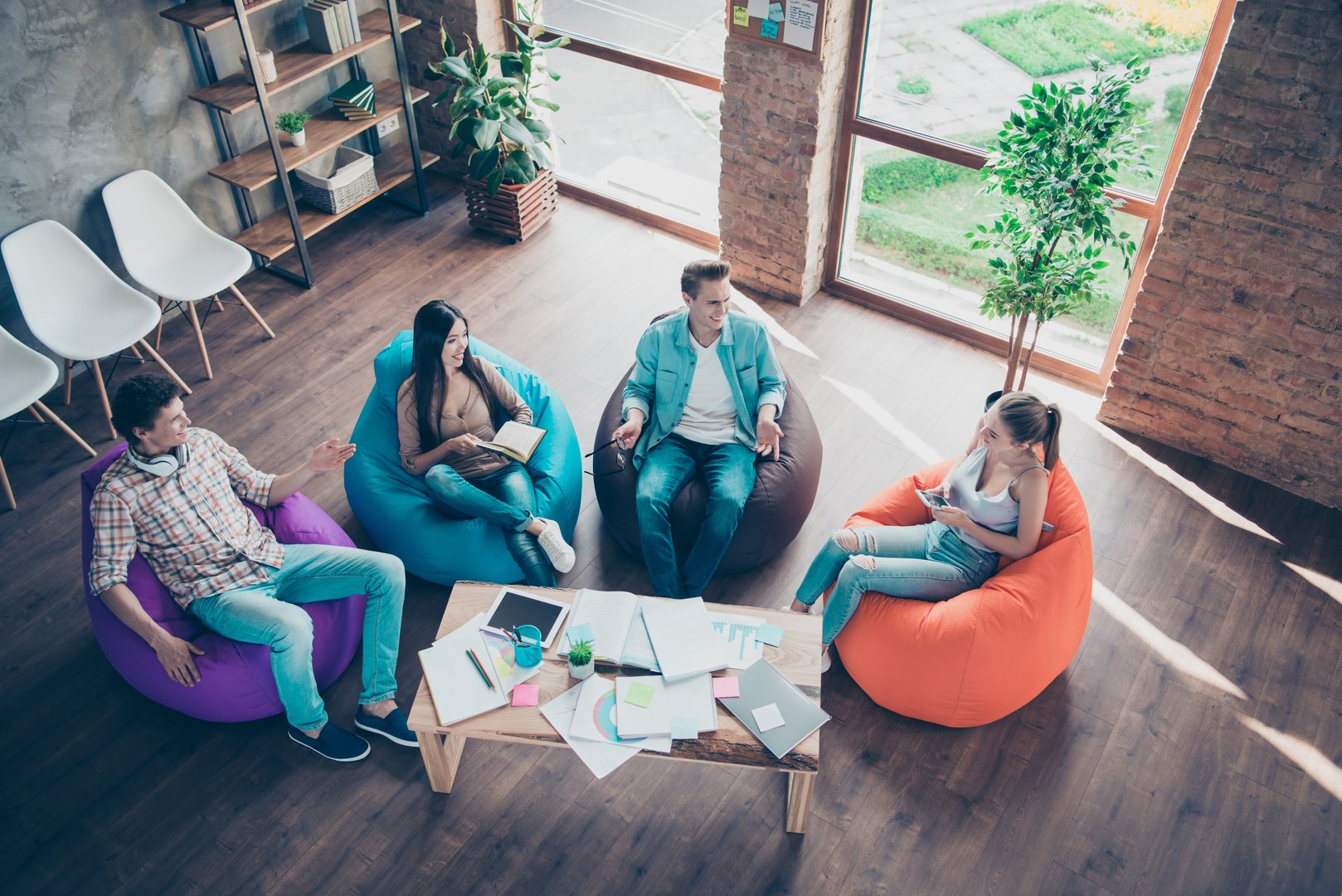 Full length, legs, body, size portrait and high angle view of workers hipster discusses success of project sitting in comfortable comfortable chairs on the table where the sheets of paper laid out