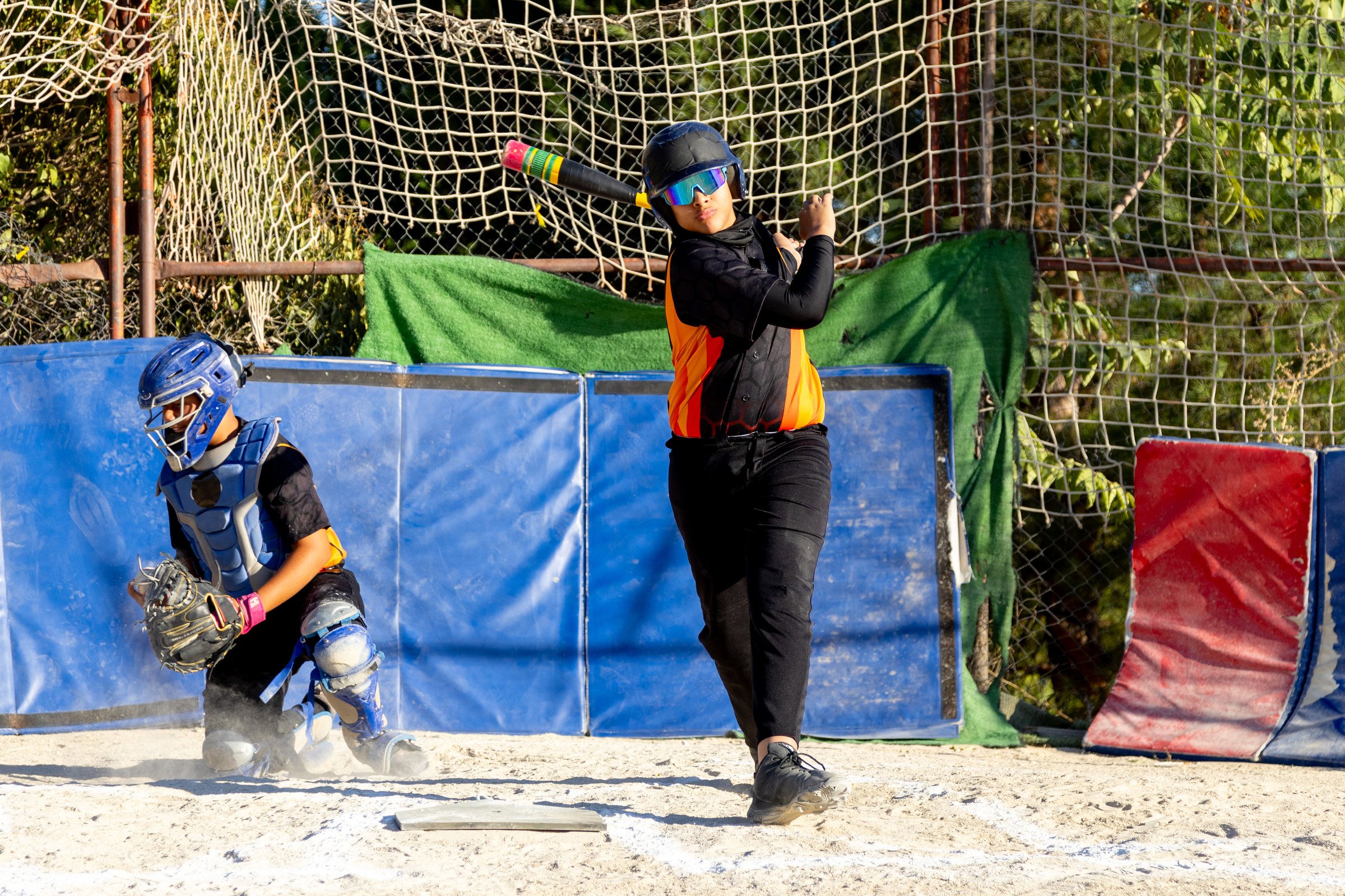 Young baseball players competing in a game. A batter swinging for a hit while a catcher is ready behind home plate