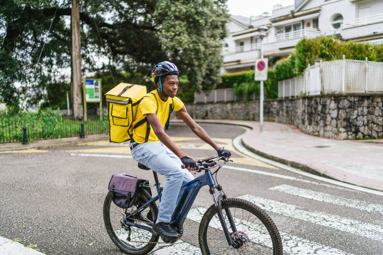 A young African delivery cyclist rides his bike through a quiet residential neighborhood. Concept of urban food delivery.