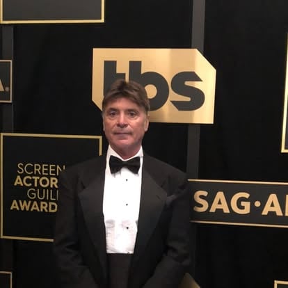 Person in a tuxedo standing in front of a Screen Actors Guild Awards backdrop.