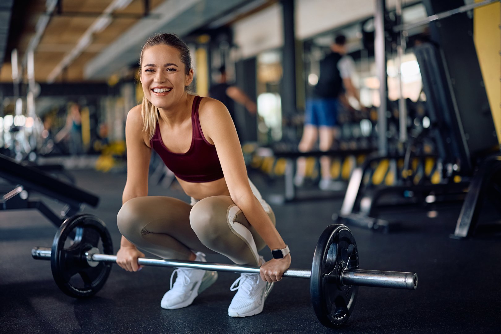 Happy female athlete exercising with barbell in a gym and looking at camera.