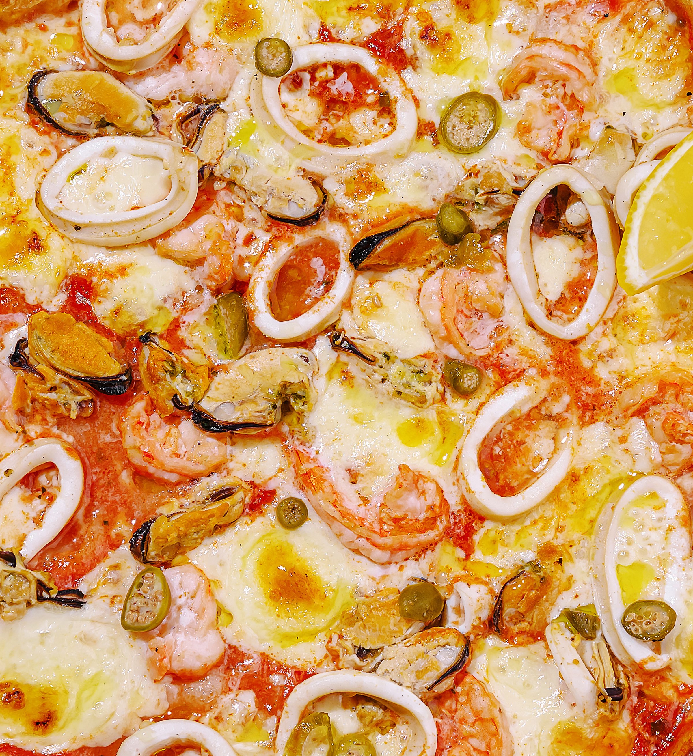 A piping hot seafood pizza is loaded with shrimp, squid, mussels, and sliced lemon. Melted cheese and a rich tomato sauce enhance the delightful flavors of this dish.