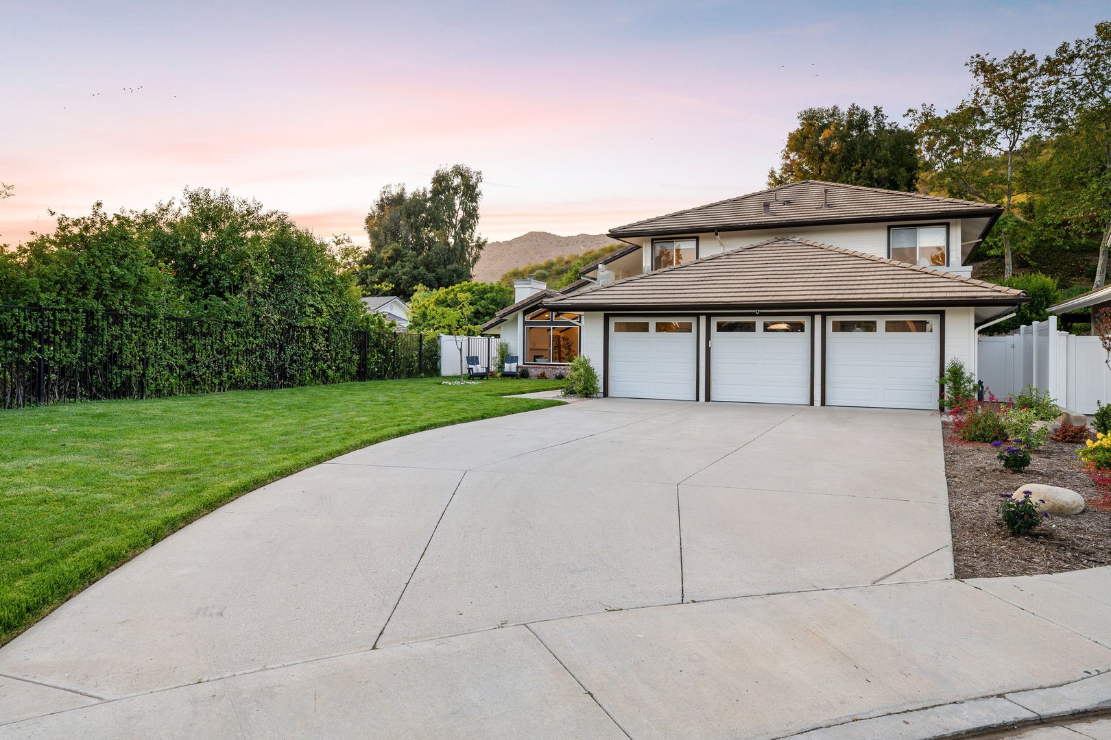 Modern suburban home with a large driveway and well-maintained lawn at sunset