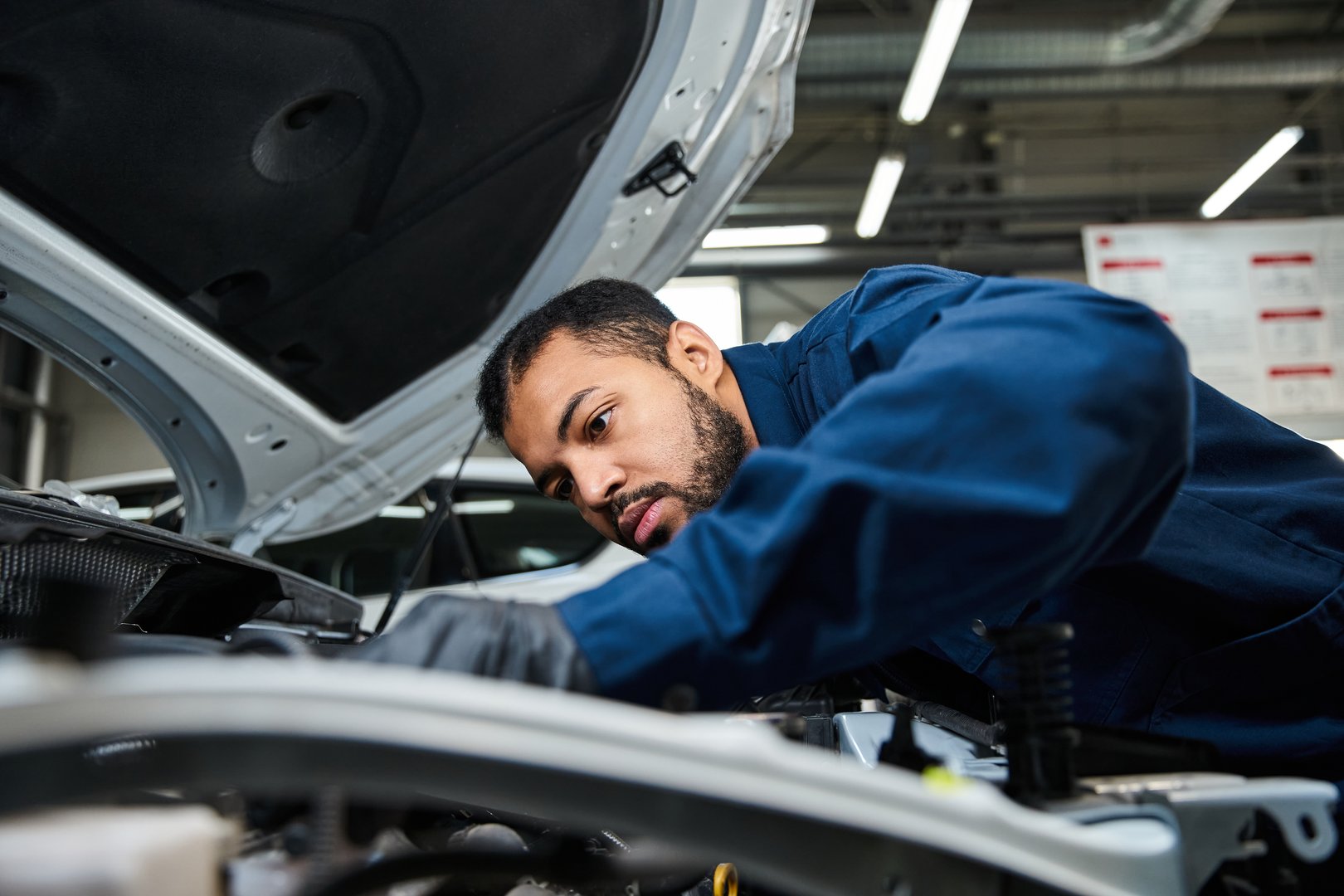 A young mechanic concentrates on car maintenance at a bustling auto repair service center.