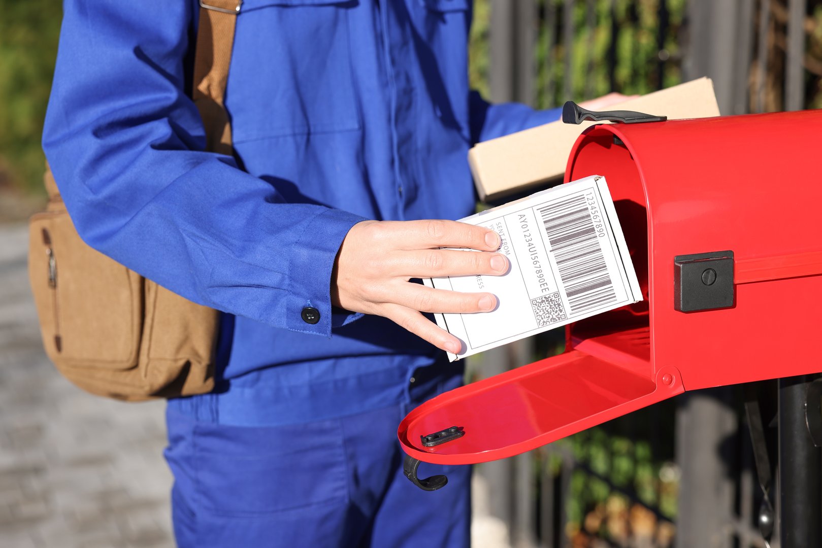 Postman putting parcel into mail box outdoors, closeup