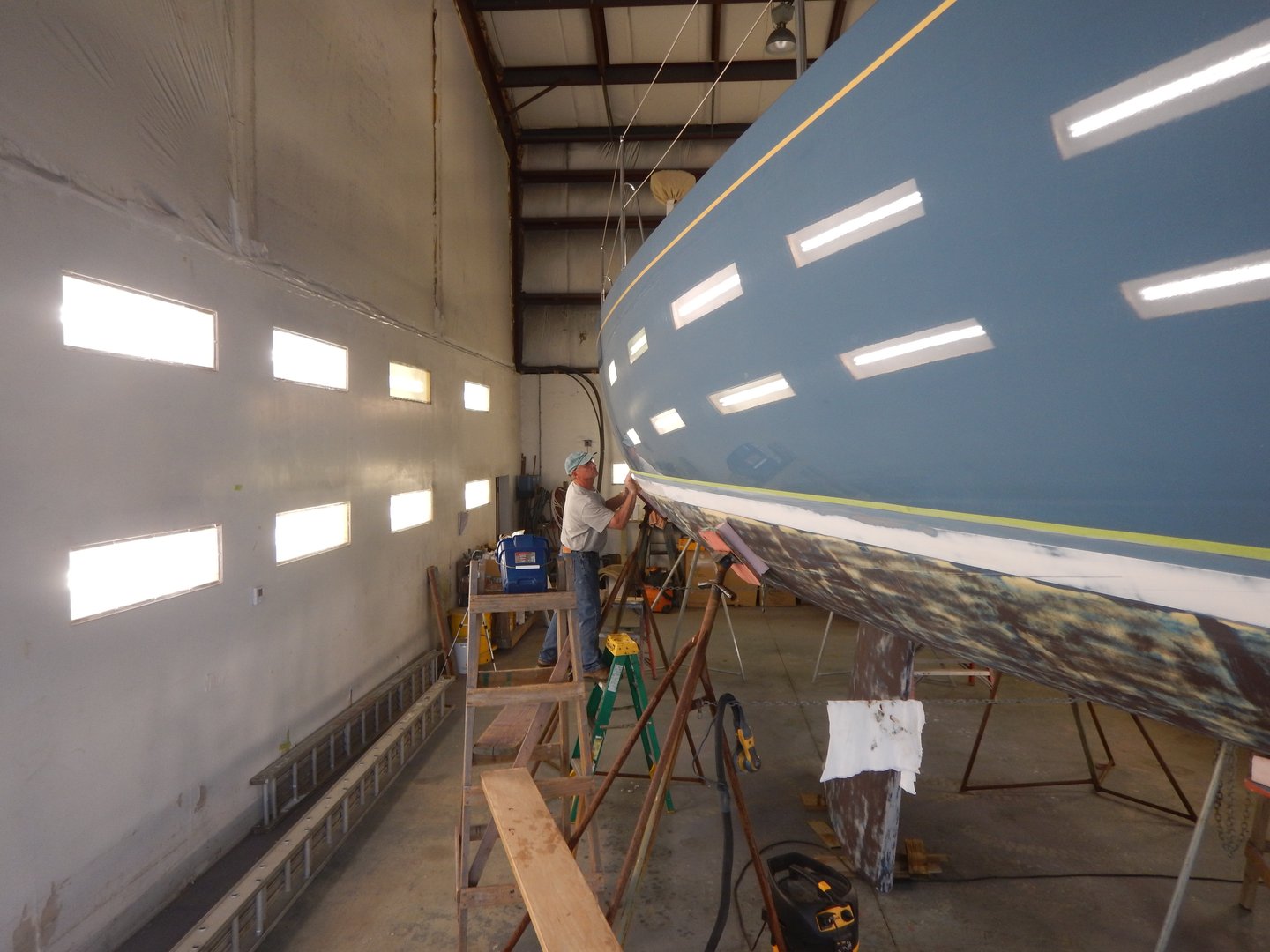 Man painting a large sailboat in a paint shed.